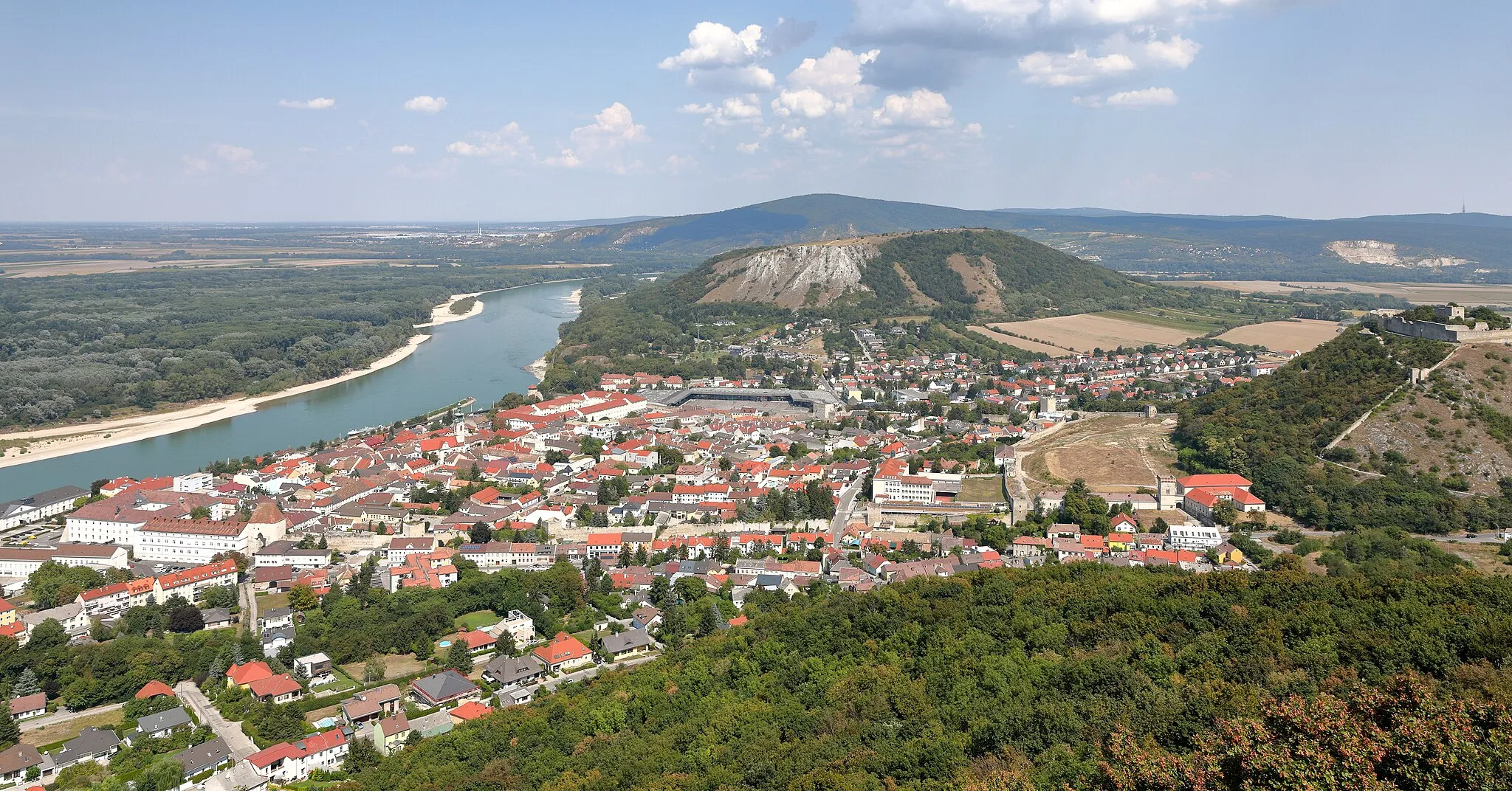 Photo showing: Blick vom Hundsheimer Berg auf die niederösterreichische Stadtgemeinde Hainburg an der Donau. Links im Bild die Donau mit der Hainburger Au, ganz rechts der 291 m hohe Schlossberg mit der Heimenburg, hinter Hainburg (Bildmitte) der 346 m hohe Braunsberg und hinter diesem der 514 m hohe Thebener Kogel (Devínska Kobyla).