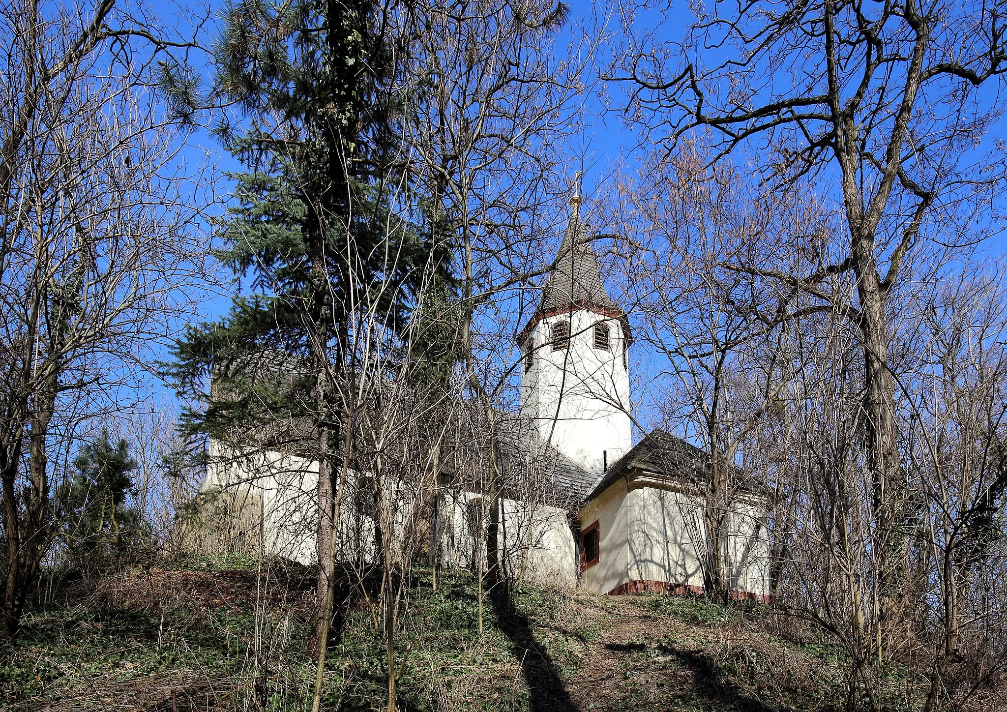 Photo showing: Südwestansicht der katholischen Filialkirche hl. Johannes in Oberhausen, ein Ortsteil der niederösterreichischen Stadt Groß-Enzersdorf. Der heutige Kirchenbau stammt urkundlich aus dem Jahr 1652/53. Er steht auf einem 7,5 Meter hohen künstlich aufgeschüttetem Erdhügel, der von einem Ringgraben umgeben ist. Hügel und Wassergraben waren ursprünglich Teil der Verteidigungsanlagen der Festung Sachsengang und wurden um das Jahr 1000 errichtet.