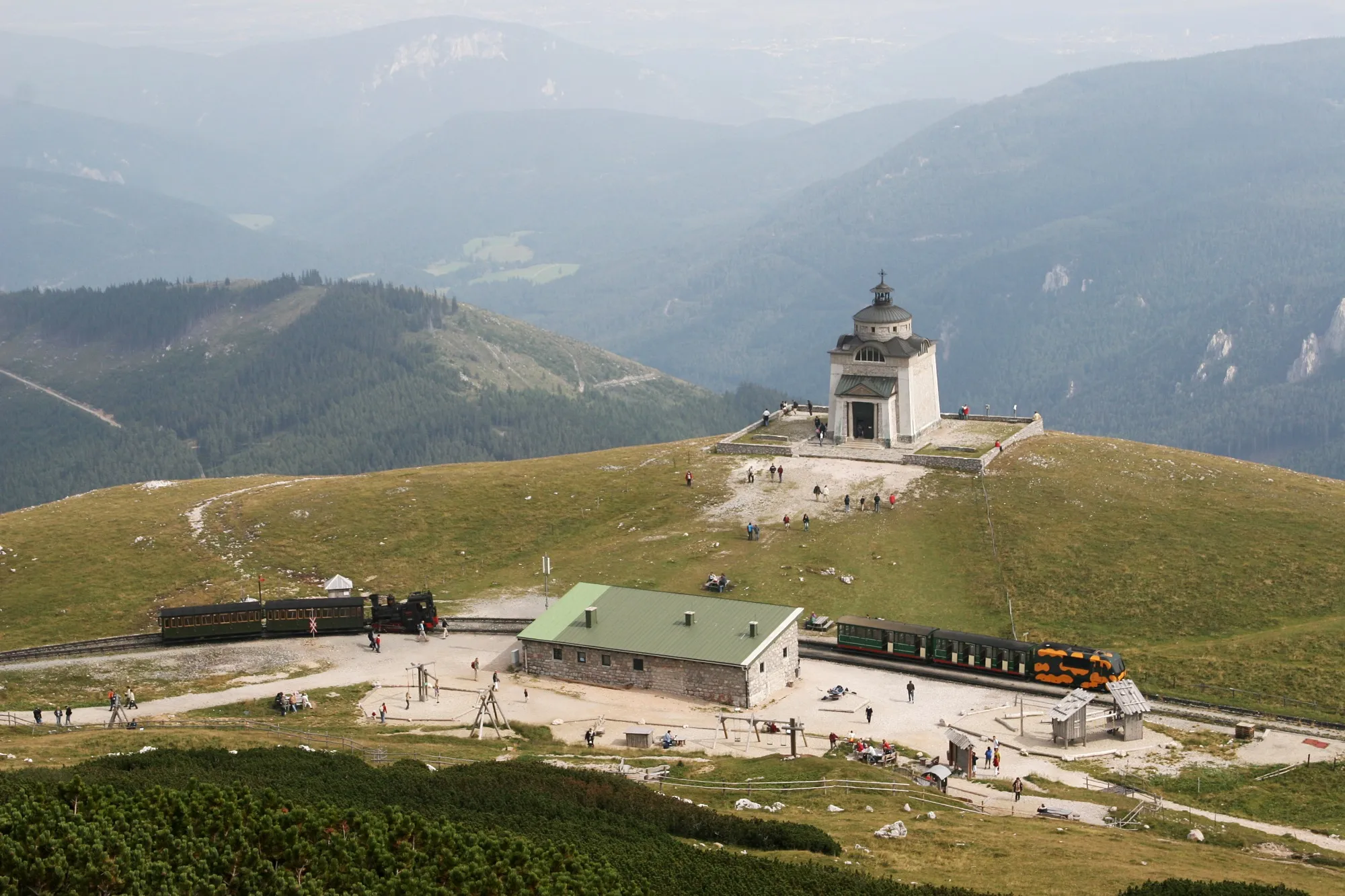 Photo showing: Hochschneeberg summit station and empress Elisabeth memorial church. In the station a steam train and a Salamander traction unit with a rake of conventional carriages can be seen.