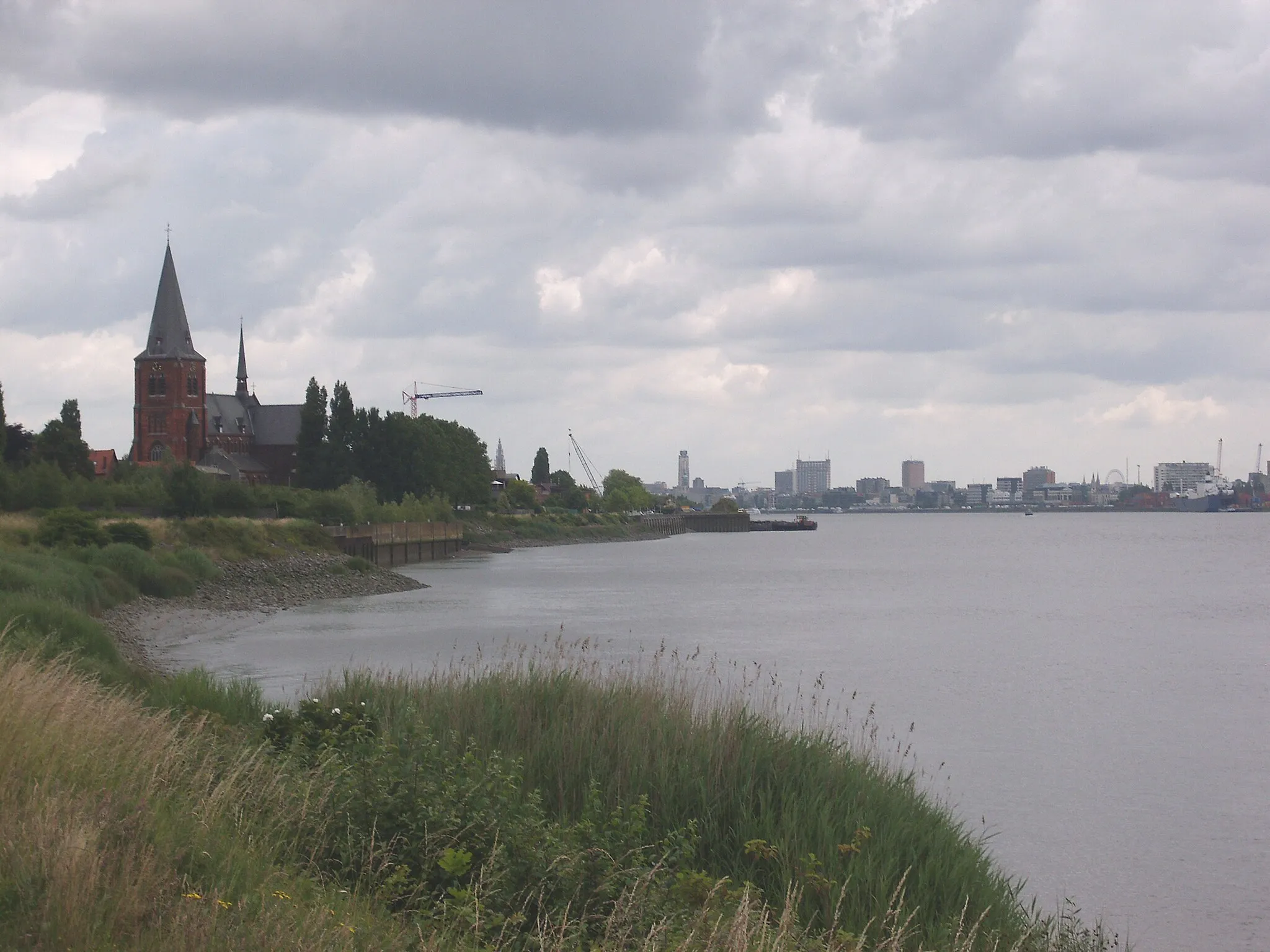 Photo showing: Zicht op Burcht aan de Schelde - op de achtergrond de stad Antwerpen - provincie Antwerpen - Vlaanderen - België
De Sint-Martinuskerk in Burcht werd op het einde van de 19de eeuw volledig afgebroken, op het gotische koor na. Op dezelfde plaats herrees een neogotische kerk (1889-1904). De kerk werd in 1940 zwaar beschadigd door een brandbom en werd na de oorlog volledig hersteld.