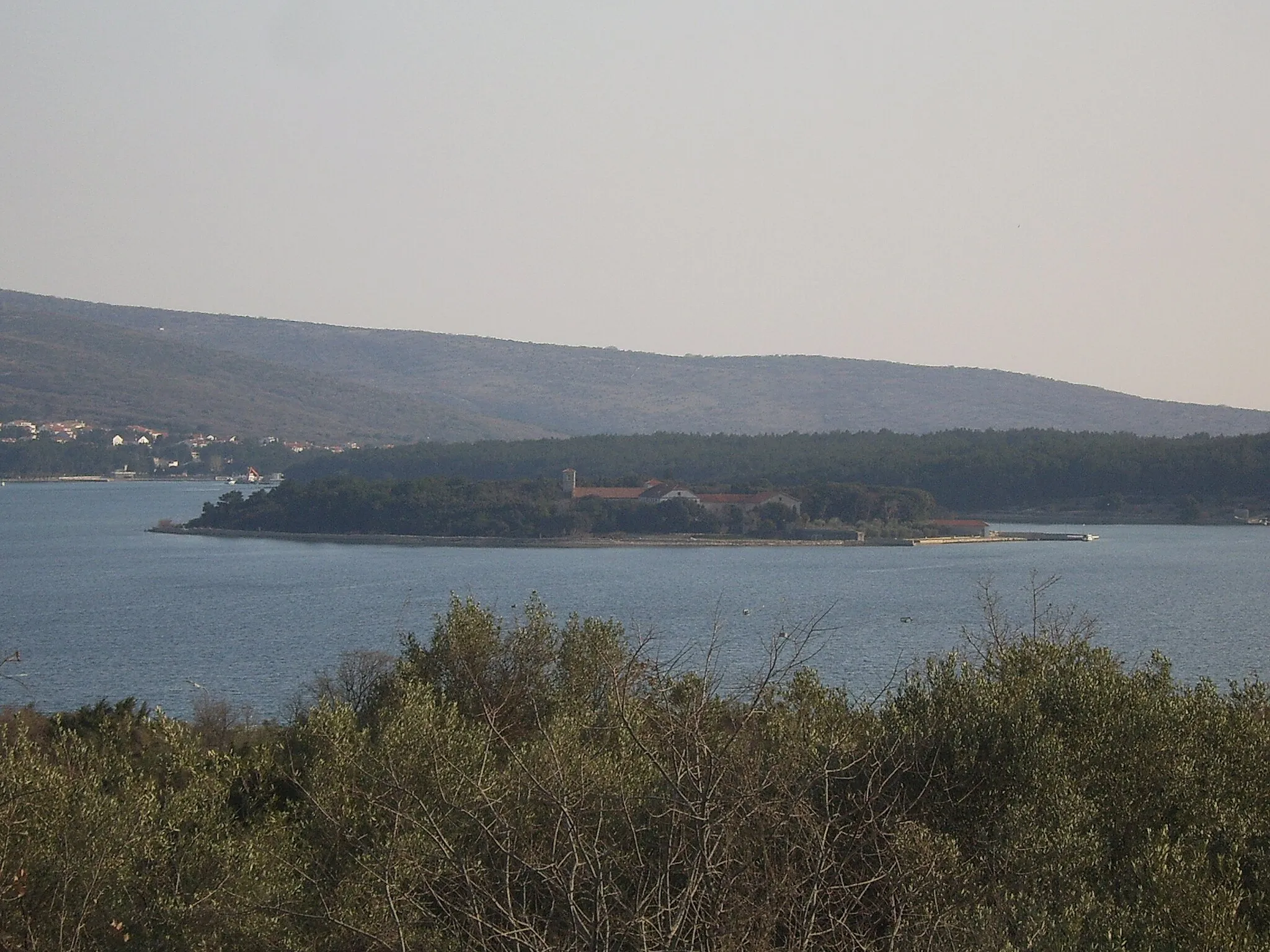 Photo showing: Otočić Košljun u Puntarskoj dragi slikan iz Kornića. U pozadini, lijevo, se djelomično vidi mjesto Punat, a desno poluotok Prniba