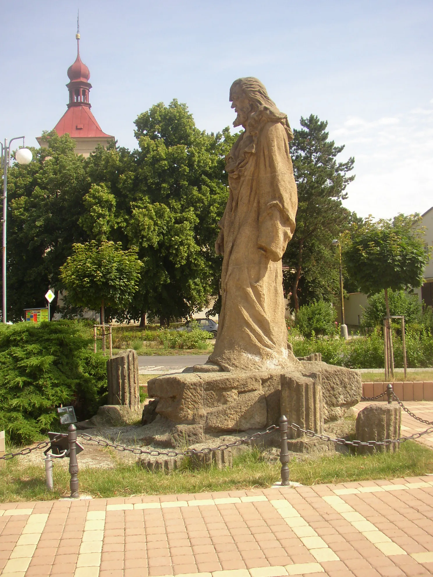 Photo showing: Bohušovice nad Ohří, Litoměřice District, Czech Republic. Jan Hus memorial in Hus Square, a 1911 work by sculptor Ladislav Beneš. A view of the left side (from the south), in the background tower of SS Procopius and Nicholas church.