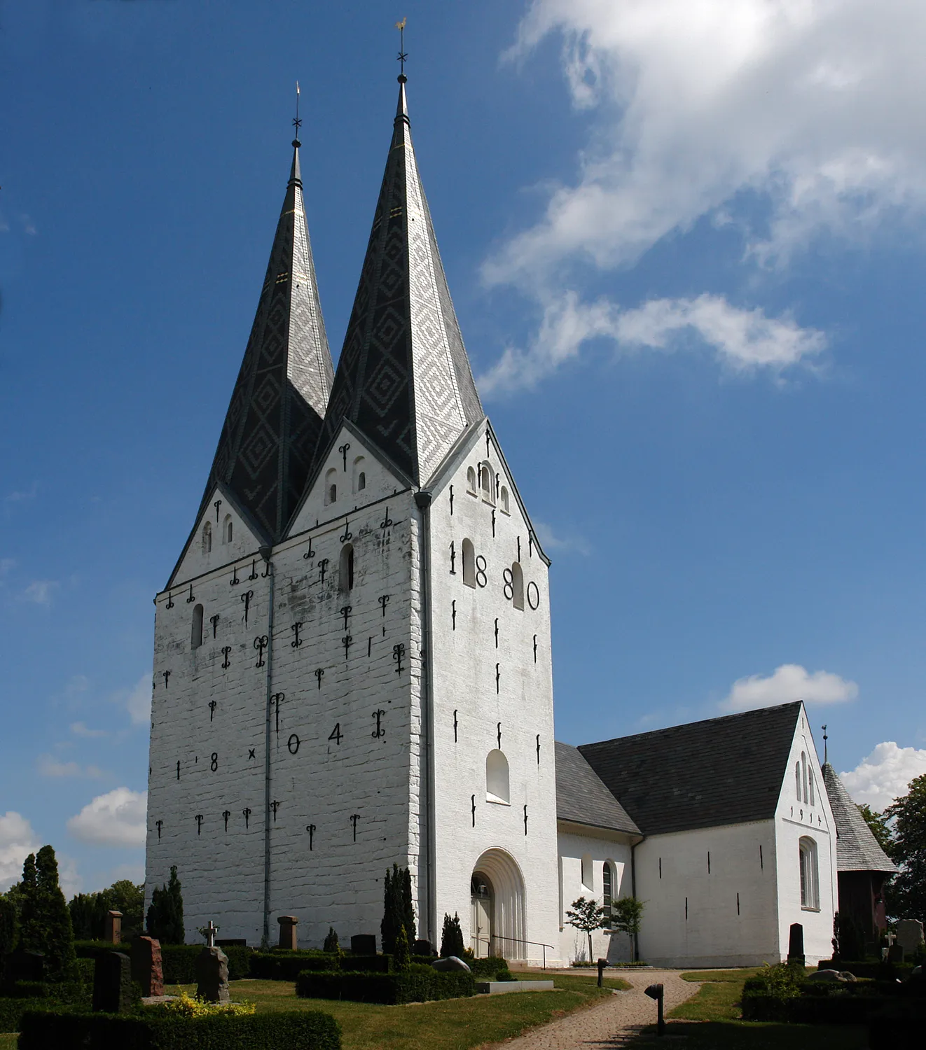Photo showing: Broager Kirke: um 1200 auf einem 40 m hohen Hügel in romanischem Stil aus Ziegeln erbaut. Der 40 m hohe Turm mit zwei Spitzen ist etwas jünger, Westmauer 1804 mit Quadern verstärkt