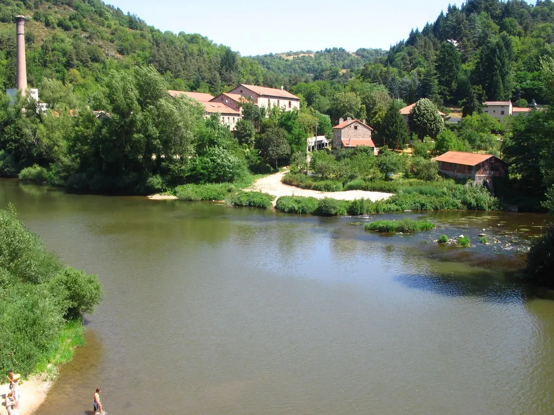 Photo showing: Confluence Lignon-Loire, cote 460, à cheval sur les communes de Beauzac, Monistrol et Saint-Maurice.
A l’activité de carrier, consistant en l’extraction de pierres de construction à l’usage du bassin stéphanois, alors en pleine croissance, vient s’ajouter en 1892 la production d’énergie hydraulique, lorsque la Cie électrique de la Loire installe une 1ère usine.
Il s’agit de fournir du courant à une vingtaine de communes environnantes, ainsi qu’à l’industrie naissante.
La cheminée de 40 m visible à l’extrémité gauche, est celle des anciennes papeteries de Pont de Lignon.
L’usine démarre en 1901 sous l’impulsion des frères A. & L. Lumière, désireux de mettre à profit la grande pureté des eaux du bassin, pour leur production de papier photographique.
Le site est repris par le groupe d’édition Hachette 25 ans après.
Vers 1950, ce sont près de 160 ouvriers qui sortent 1 800 t de papier à l’année. Production expédiée dans le monde entier via la gare de Confolent, sur l’axe Le Puy-Saint Etienne.
Une réorientation s’opère vers 1969-75, les préparations pour papier peint côtoient leur homologue glacé des magazines... jusqu’aux paquets d’un célèbre cigarettier tricolore.

Diverses activités ensuite jusque 2002, parfois en lien avec les loisirs (assemblage d’ULM...), avant fermeture définitive.