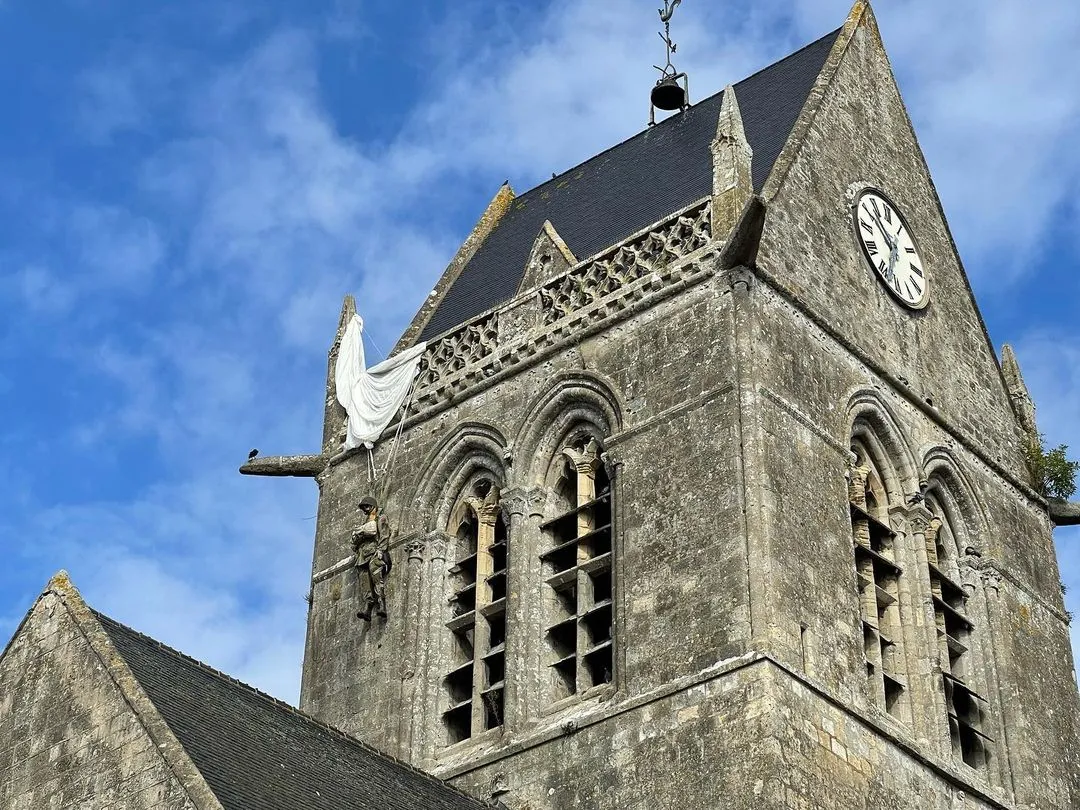 Photo showing: Église de Sainte-Mère-Église, avec un mannequin de parachutiste (John Steele) accroché au clocher.