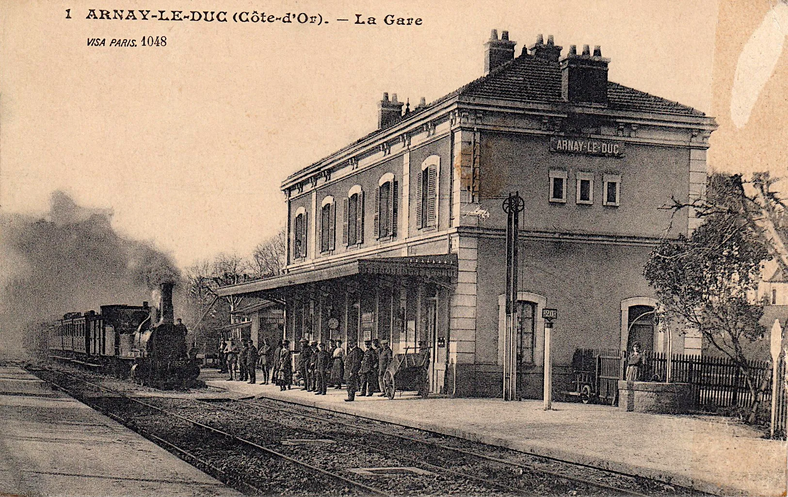 Photo showing: Arnay-le-Duc (Côte-d'Or): General view of the station with travelers on the platform and the steam locomotive arriving in the station.