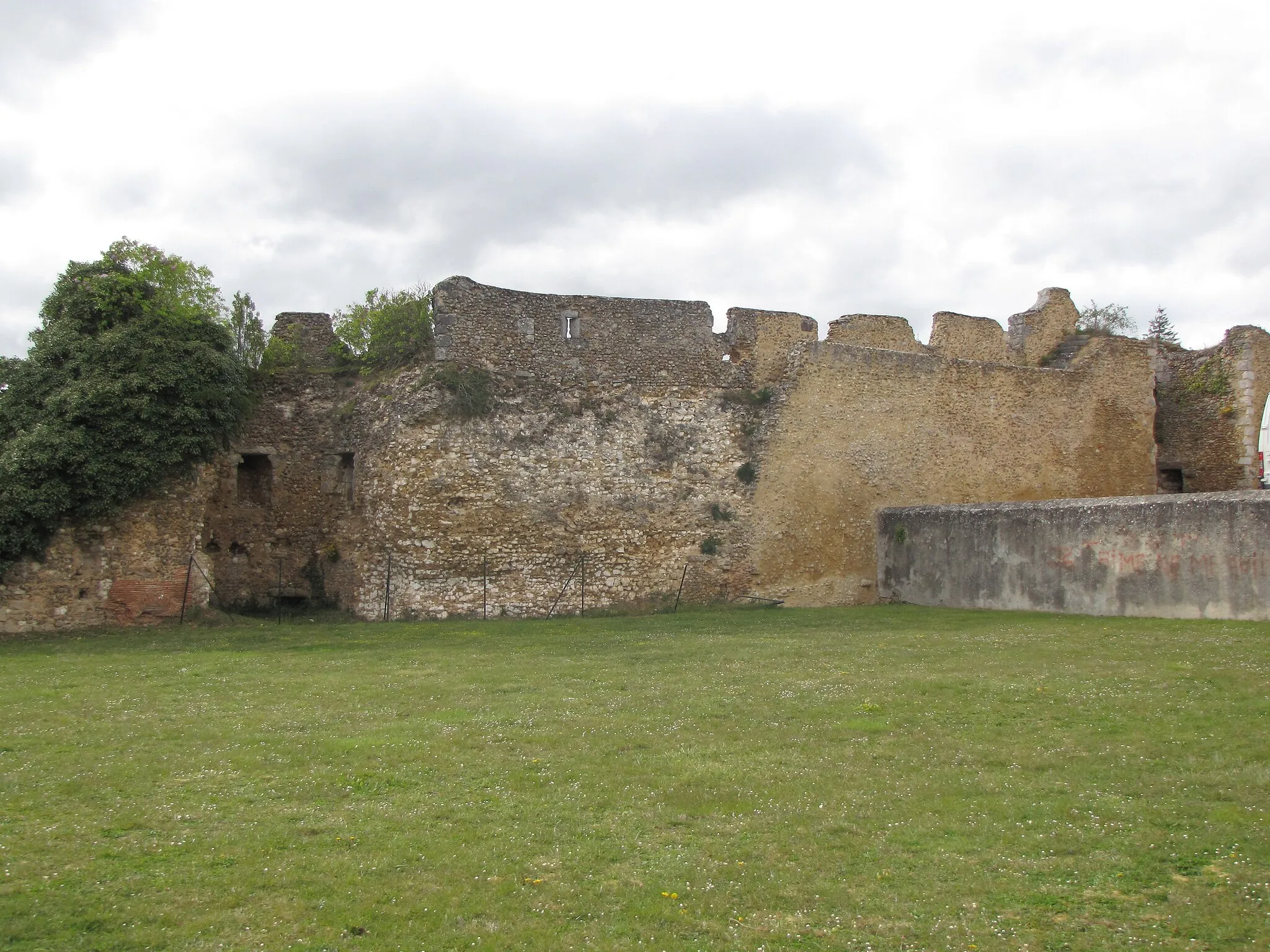 Photo showing: Looking north-west from the center of the panorama place at the château-haut, we see part of the west battlements of the castle. These remnants of fortifications include here two towers and their curtain wall, with part of the chemin de ronde and some crenels. The red gate leading downtown is immediately after the tower on the right
The tower on the left still shows the holes in which were set the beams supporting a floor. Their height, or lack thereof, tells that the actual ground of the inner courtyard was quite a way deeper than it is now. On the left hand-side of the same tower, the wall shows some brickwork that tells of a door, now walled-in and nearly buried.