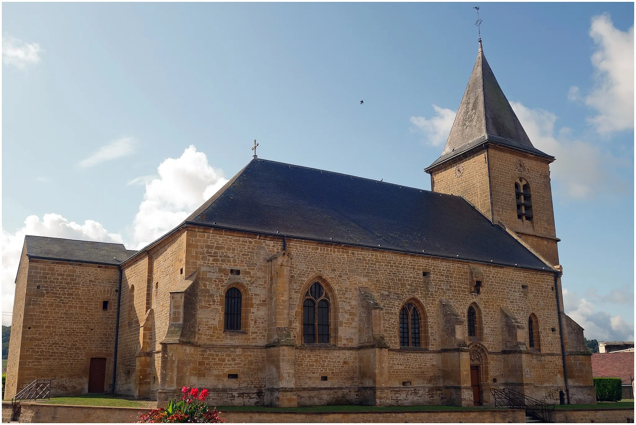 Photo showing: Aux abords de la Meuse, l'église Notre Dame du XVIe siècle possède une tour-porche et au niveau du chevet un bâtiment percé d'orifice de feux. De petites canonnières de fortifications sont encore visibles sur les bas-côtés.