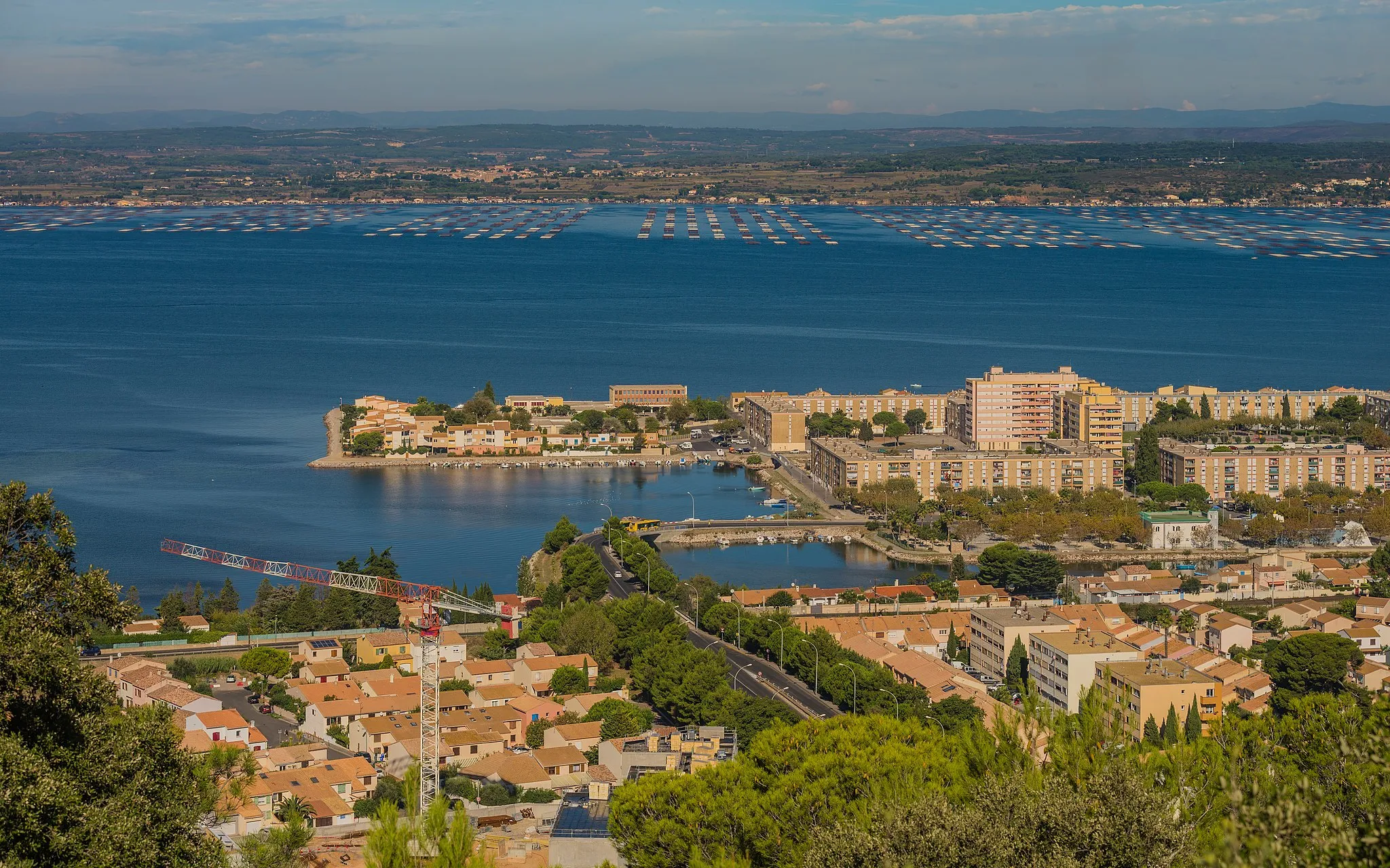 Photo showing: In the foreground the Southwestern part of the Ile de Thau Neighbourhood and the Étang de Thau.  In background on the opposite bank the commune of Loupian and its oyster farms. Sète, Hérault, France.