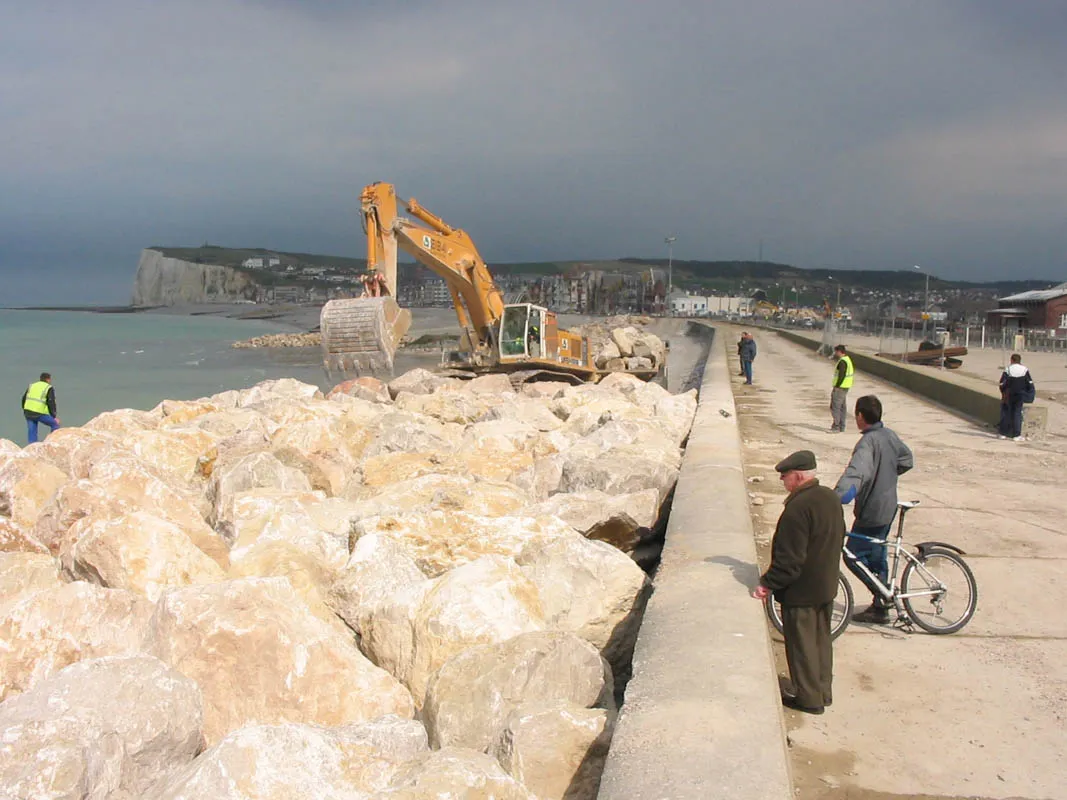 Photo showing: A wave breaking talus is beeing set up in Mers-les-Bains. An excavator is moving the rocks to build the talus.