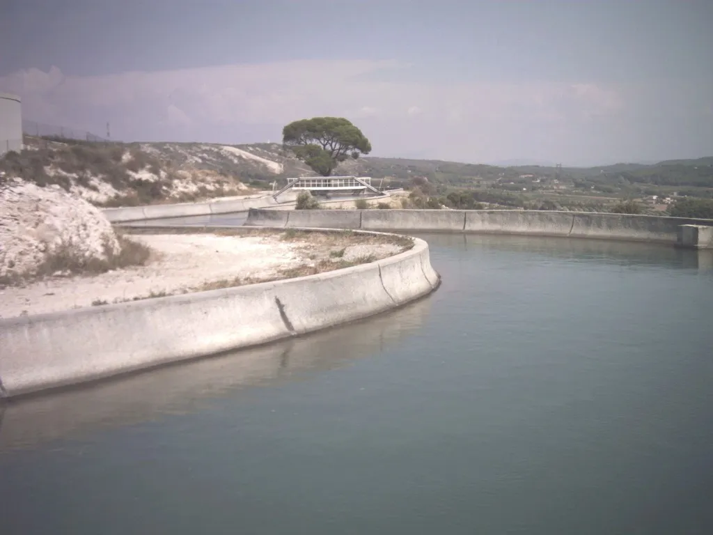 Photo showing: Le canal au nord de Coudoux, longeant le flanc de la barre de coteaux. Vue vers l'est. On aperçoit à gauche du canal une partie de cuve appartenant à l'ensemble de la station d'épuration immédiatement au nord de Coudoux. Le fleuve Arc coule au pied des coteaux.