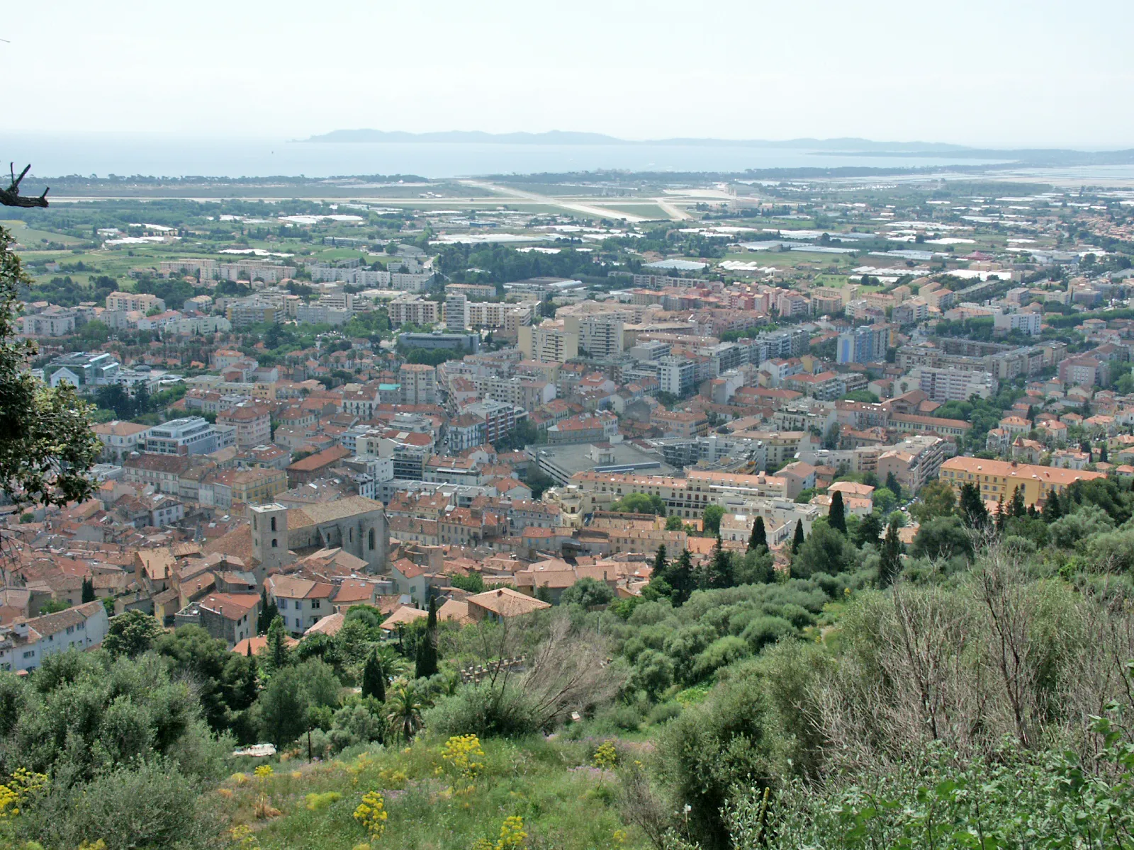 Photo showing: Hyères, vue prise du château en direction du sud. On aperçoit sur la gauche une partie de la vieille ville avec l'église Saint-Paul. En arrière-plan, les pistes de l'aéroport de Toulon-Hyères, sur la droite, la presqu'île de Giens et tout au fond l'île de Porquerolles.