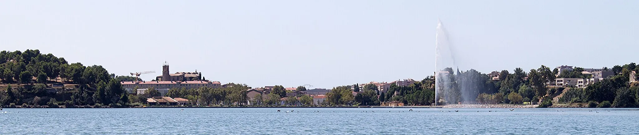 Photo showing: Berges de l'étang de l'Olivier à Istres. Vue sur le jet d'eau de l'étang et l'église Notre Dame de Beauvoir