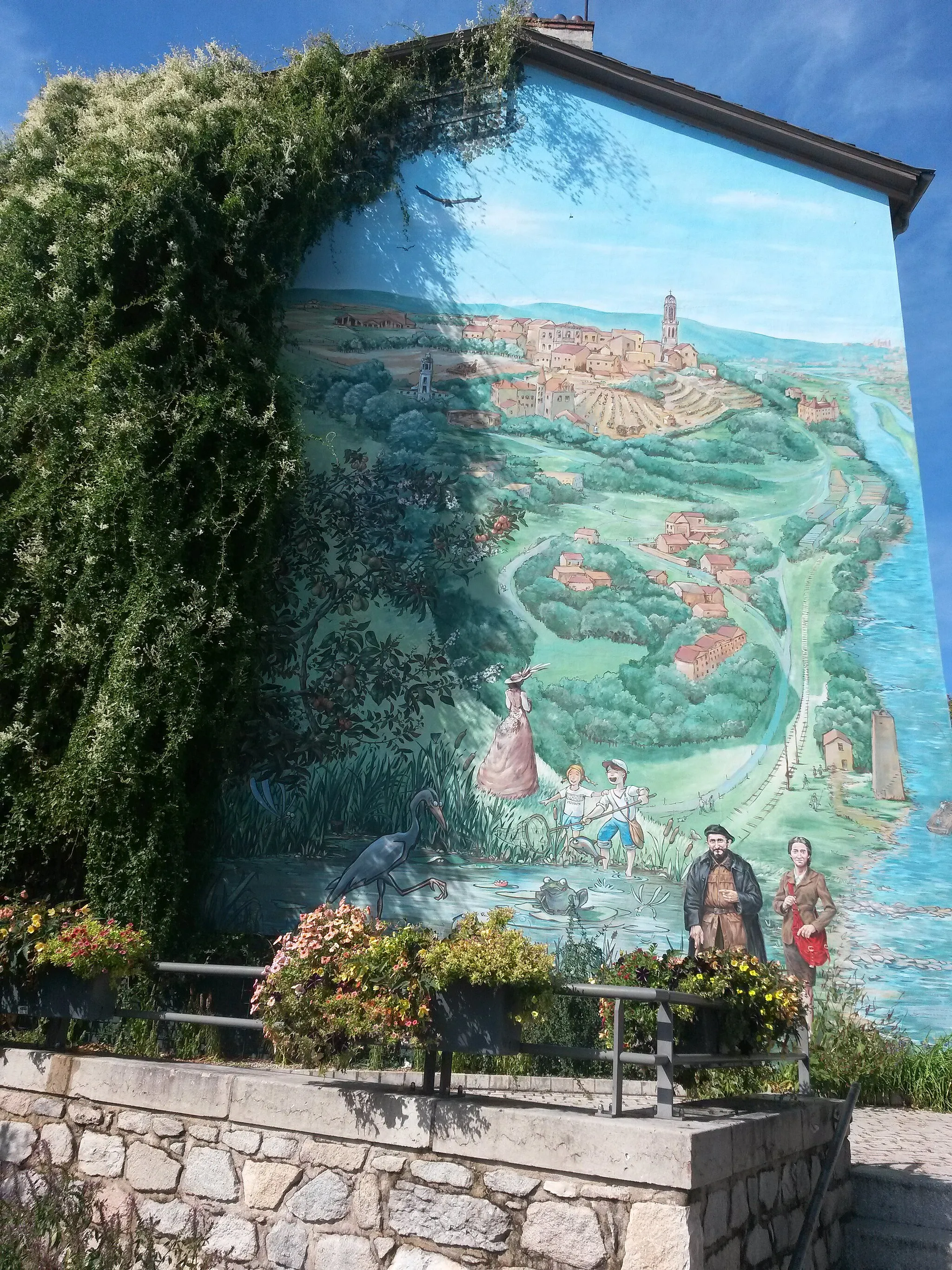 Photo showing: Photo de la fresque murale d'Irigny inaugurée en 2009. Elle mêle peinture, végétaux et lumière.
Il s'agit d'une représentation de la commune avec les monuments et les personnages notables (clocher, châteaux, tour de traille... Abbé Pierre, Daisy Georges Martin, Marie-Dorothée Petit (de dos)...).