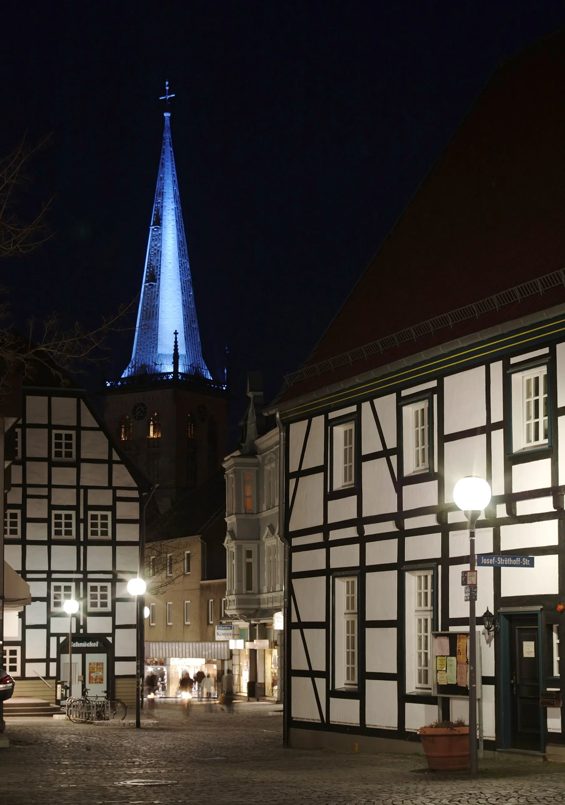 Photo showing: Stadtkirche Unna, Nordrhein-Westfalen. Nachts wird die kupferne, grünspangefärbte Turmhaube mit blauen Scheinwerfern angestrahlt. Blick von der Hertinger Straße in Richtung Alter Markt, im Vordergrund rechts das denkmalgeschützte "Fäßchen".