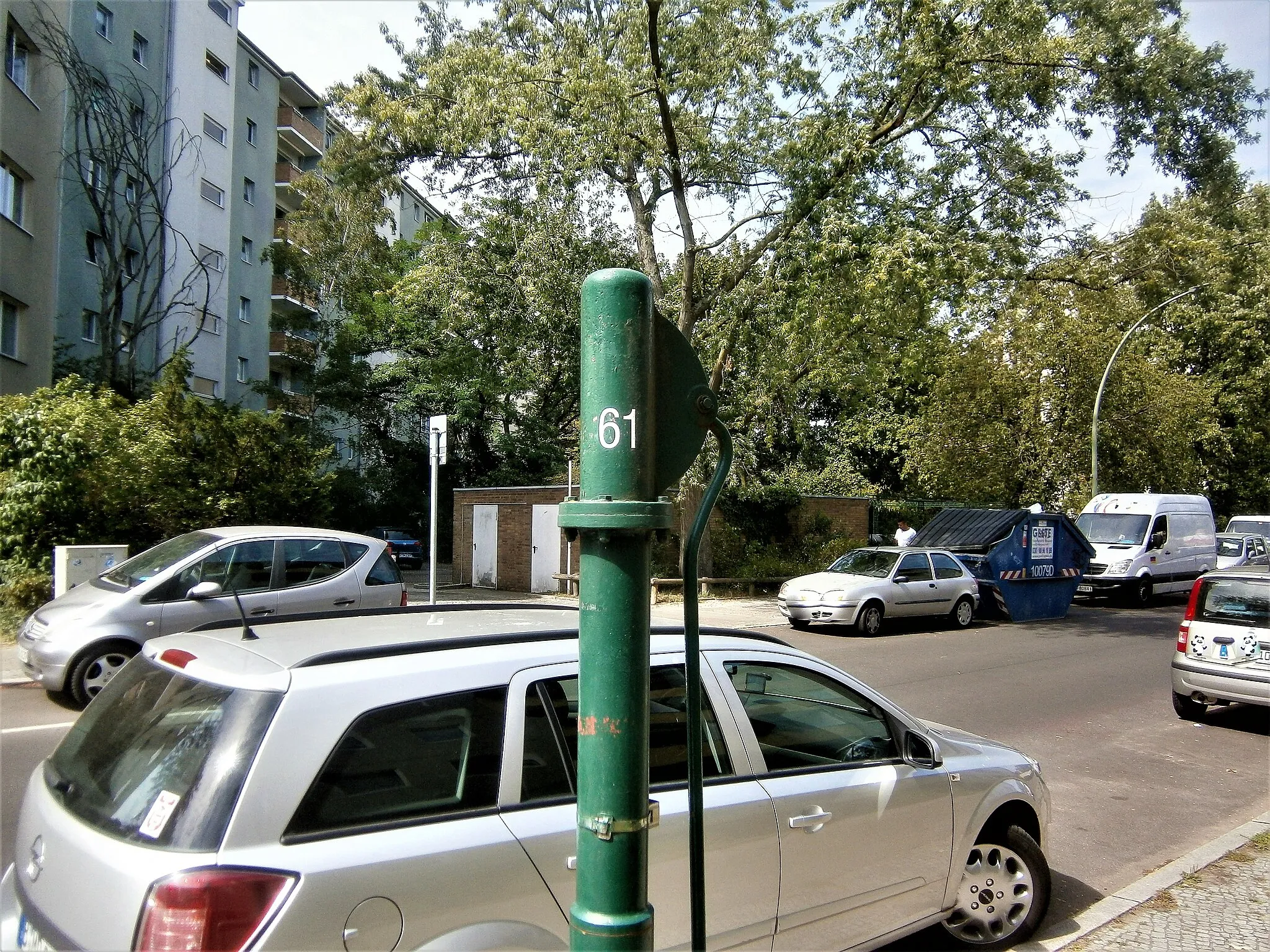 Photo showing: Der Standort des Brunnens zwischen Haakezeile und Pfefferweg ist mit Hausnummer 8 (Wohnzeile 4–8) in der Liste benannt. Ein FSH-Brunnen steht 2008 am östlichen Gehweg, allerdings vor dem viergeschossigen Wohnhaus 16 (Wohnzeile 16–20). Der (vermeintliche) Abstand beträgt dabei 60 Meter, wobei zwischen dem Haus 8 und 16 die Zufahrt zum querstehenden Block 10–14 liegt, sowie die Müll-/ Recyclingcontainer und eine Garagenreihe.[1] Die Wohnhäuser im Karree wurden in den 1960er Jahren erbaut, der Brunnenstandort könnte wohl zu diesem Zeitpunkt festgelegt sein. Der Brunnen hat für den Wasseraustritt eine lange Hülse am Schaft. Der Abfluss erfolgt unmittelbar auf den Gehsteig. Um den Brunnenfuß, der am Flansch des Sockelrohrs verschraubt ist, liegt in einer Kleinpflasterung.