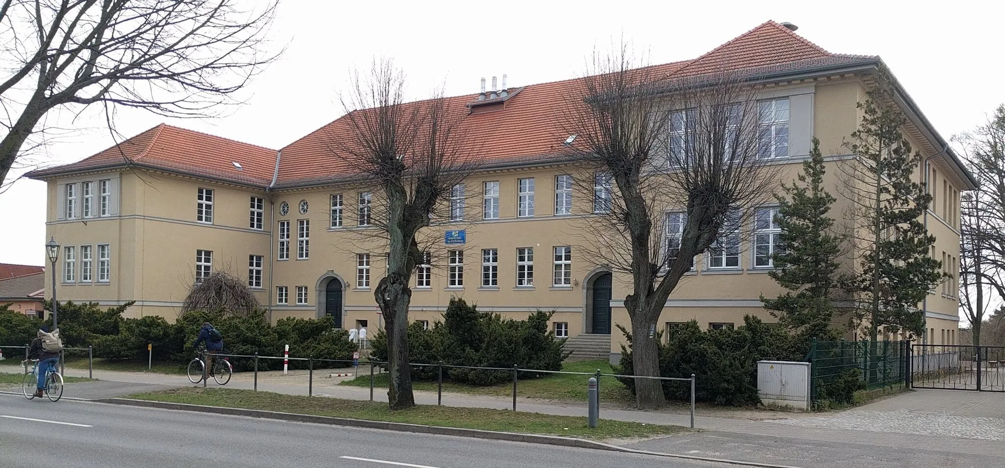 Photo showing: The school in Bahnhofsstraße 9-12, 16359 Biesenthal, Germany, is a listed building of the state of Brandenburg; Architect Otto Kuhlmann (1873-1948), start of construction August 1923, inauguration 7th March 1925.
Municipal architect Rüter (1927) gives the following description of the new and then very modern school building:
"The floor plan of the school building has a U-shape and is oriented in such a way that the two side wings are facing east and west, the open side of the U at the Bahnhofstraße, lies to the north.
The building contains a boys' and a girls' section with 7 classes each. It also includes: a teachers' room, a female teachers' room, a rector's room with an anteroom, a conference room, a room for the school doctor with an anteroom, in the boys' and girls' department each a room for the teaching materials, a drawing room with 2 model rooms, an auditorium and a gymnasium. In the basement of the girls' department is a school kitchen and milk counter, in the boys' department a bathhouse is provided, consisting of 3 baths and 16 shower baths with a dressing room. The bathhouse is also accessible to the citizens of Biesenthal. The flush toilets with water flushing are also installed in the basement. An apartment of the caretaker and 2 rooms for the public libraty are arranged on the ground floor at the main entrances.
Each department has a separate entrance. Since for the position of the classes the east and west position is to be considered as the best, the classes of the girls' section are oriented to the east, that of the boys' section to the west. The common areas such as the gymnasium, the auditorium, the drawing room are arranged between the two departments, in the middle. The gymnasium is located to the schoolyard, one level above ground, and extends through the lower and ground floors. It has a length of 17.00 m and a width of 10.50 m; on both narrow sides are each a device and changing room. Above the gymnasium, also to the south, is the auditorium and, to the north, the drawing room with model rooms. Rector's and teachers' rooms are arranged so that the schoolyard can be overlooked from there.
The classrooms are designed for 40 students, they have a size of 7.10 m to 5.65 m. The clear height is 3.60 m, so that an exposure to the last place is guaranteed. Like the classes, the corridors, which are 2.30 meters wide, are light and airy. In each section 2.00 m wide staircases lead from the basement to the upper floor, where the staircase against the corridors is completed by a rich, architecturally effective wooden latticework interspersed with figures of the fairy tale world.
The architecture of the auditorium is kept in tight classical forms, which is effectively supported by a well-coordinated surface painting. The ceiling has received a richer stucco, which contributes significantly to the lifting of the festival room. For eventual evening lighting serve 1 larger and 2 smaller bronze chandeliers with a total of 51 lamps.
All school rooms are heated by a low-pressure steam heater, the caretaler apartment and the library by a Narag heating system. Each class is vented by an exhaust duct of an appropriate profile .
All wastewater is purified by a fresh water treatment plant and then fed to the nearby Sydow stream. "

Text from: Oberbarnimer Kreiskalender 1927, 16th year, edited by Rudolf Schmidt, pages 44-46.