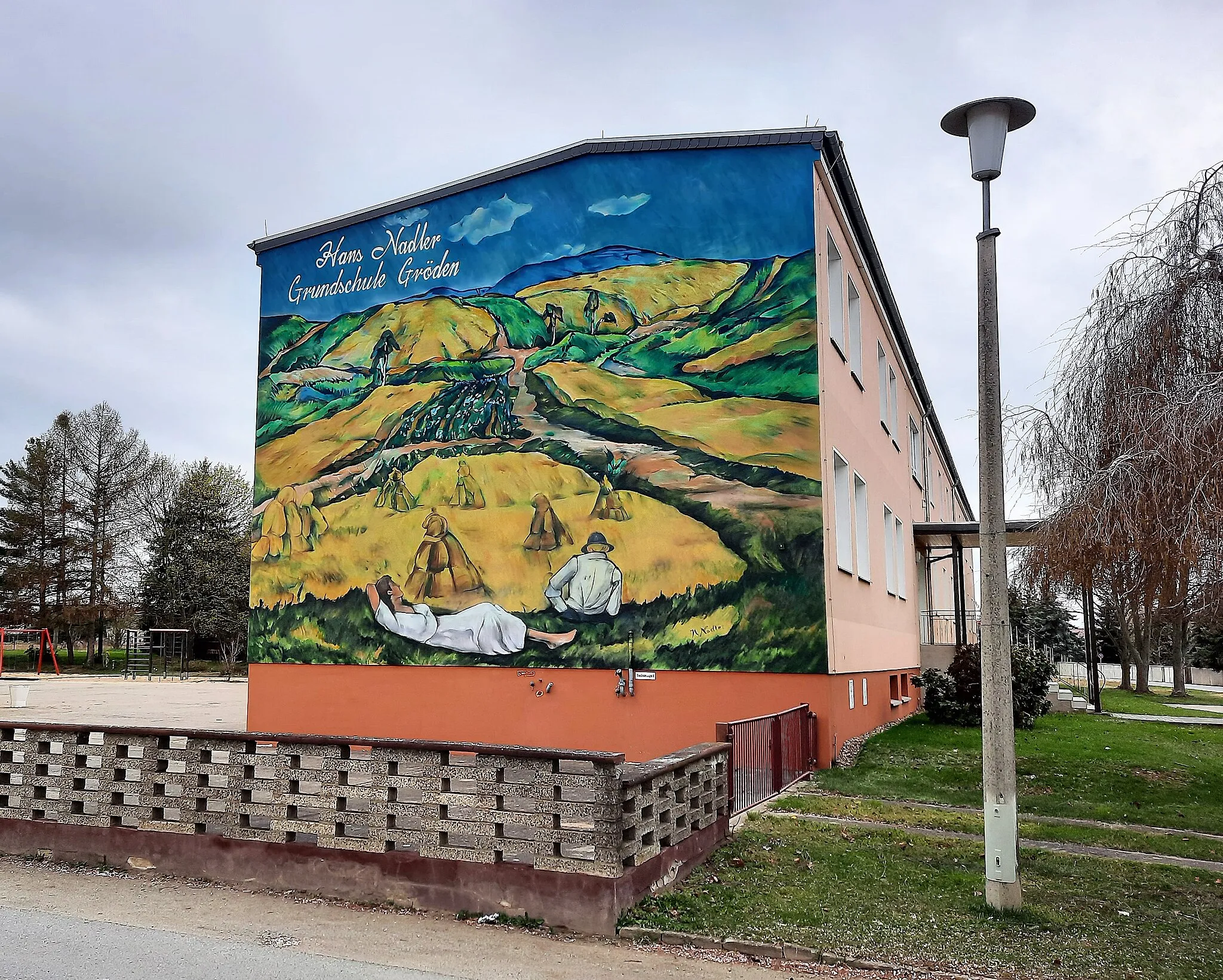 Photo showing: Die Hans-Nadler-Grundschule in Gröden. Die Giebelwand des Gebäudes ziert ein Graffito des Dresdner Künstlers Christian Weiße, das das Gemälde „Schradenlandschaft“ von Hans Nadler zeigt, welches durch den Künstler maßstabsgetreu auf die Fassade übertragen wurde.