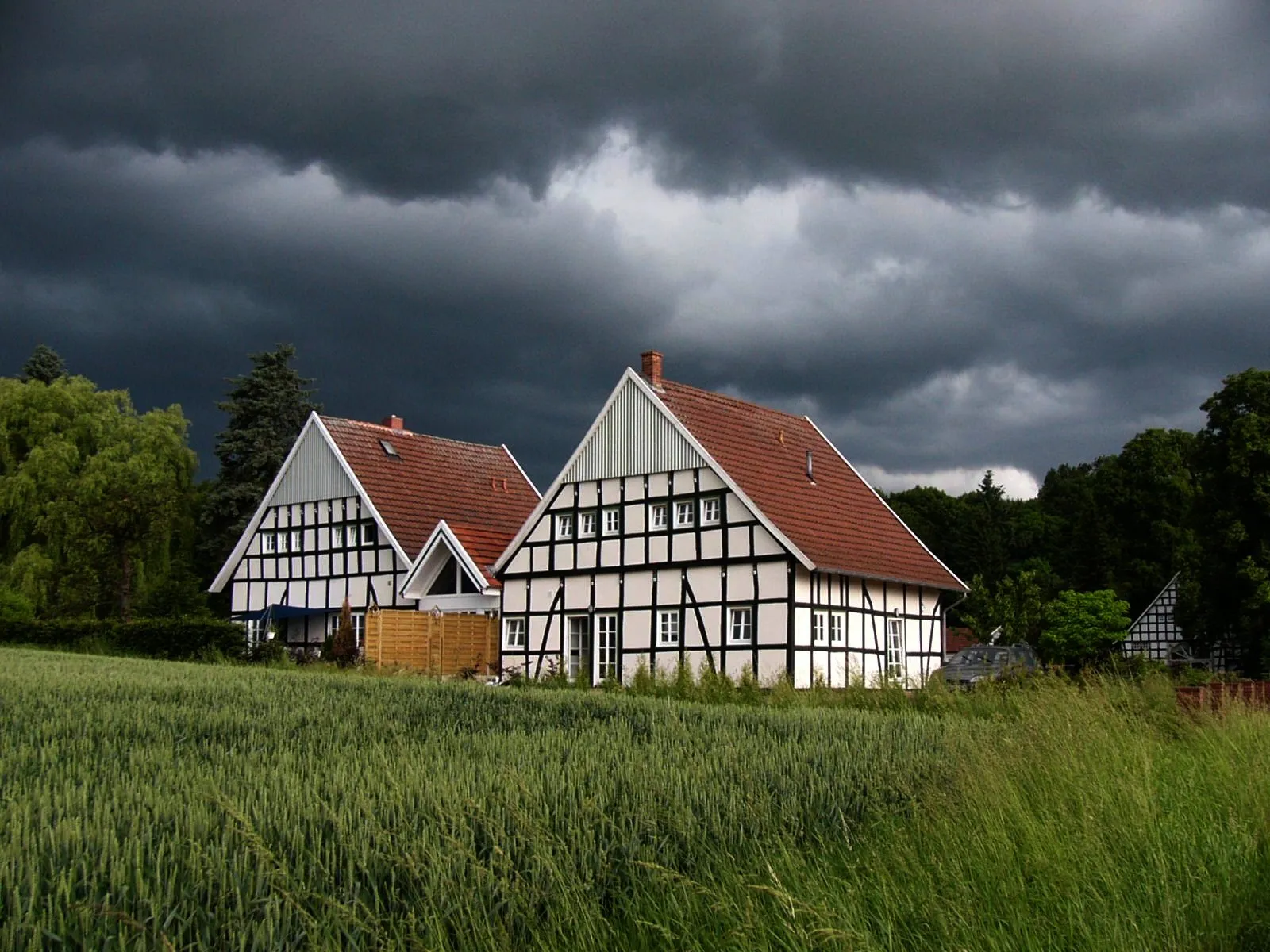 Photo showing: Two refurbished houses of type "Kotten" on their original site in Hüllhorst, Minden-Lübbecke, North Rhine-Westphalia, Germany in a storm; at right in the background is a large timbered house belonging to the large farm in Ostwestfalen of which the Kotten were part of.