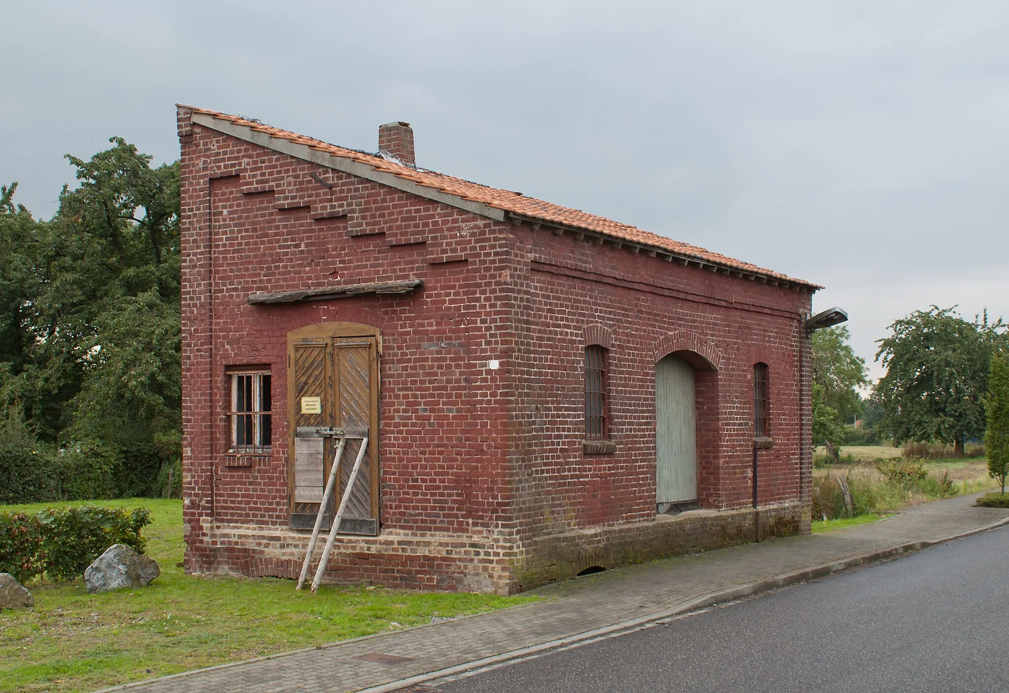 Photo showing: Betriebsgebäude der Geilenkirchener Kreisbahnen im Bereich des ehemaligen Bahnhofs Gangelt. Rechts neben dem Schuppen, im Verlauf der heutigen Straße, lagen die Bahnhofsgleise.
Das Bauwerk ist das letzte originale betriebliche Gebäude der Geilenkirchener Kreisbahnen.