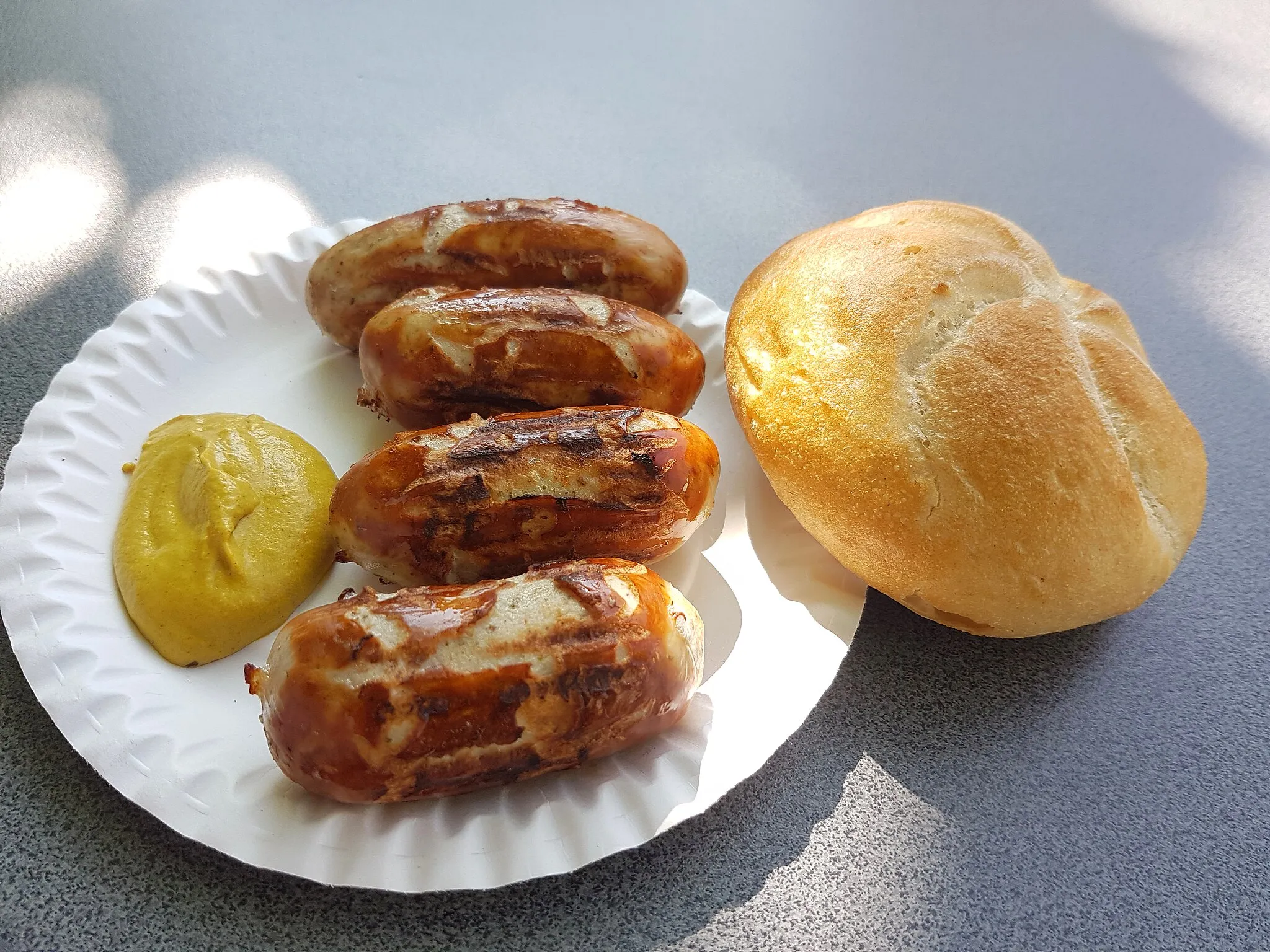 Photo showing: Original Brunner's sausages from the Brunner butchery in Landshut. The sausages are sold at snack stands in and around Landshut. They are grilled on charcoal and eaten with mustard and bread rolls or pretzels. One usually orders one pair, or 2 pairs of sausages. Photographed at a sausage stand in Ergolding opposite the town hall.