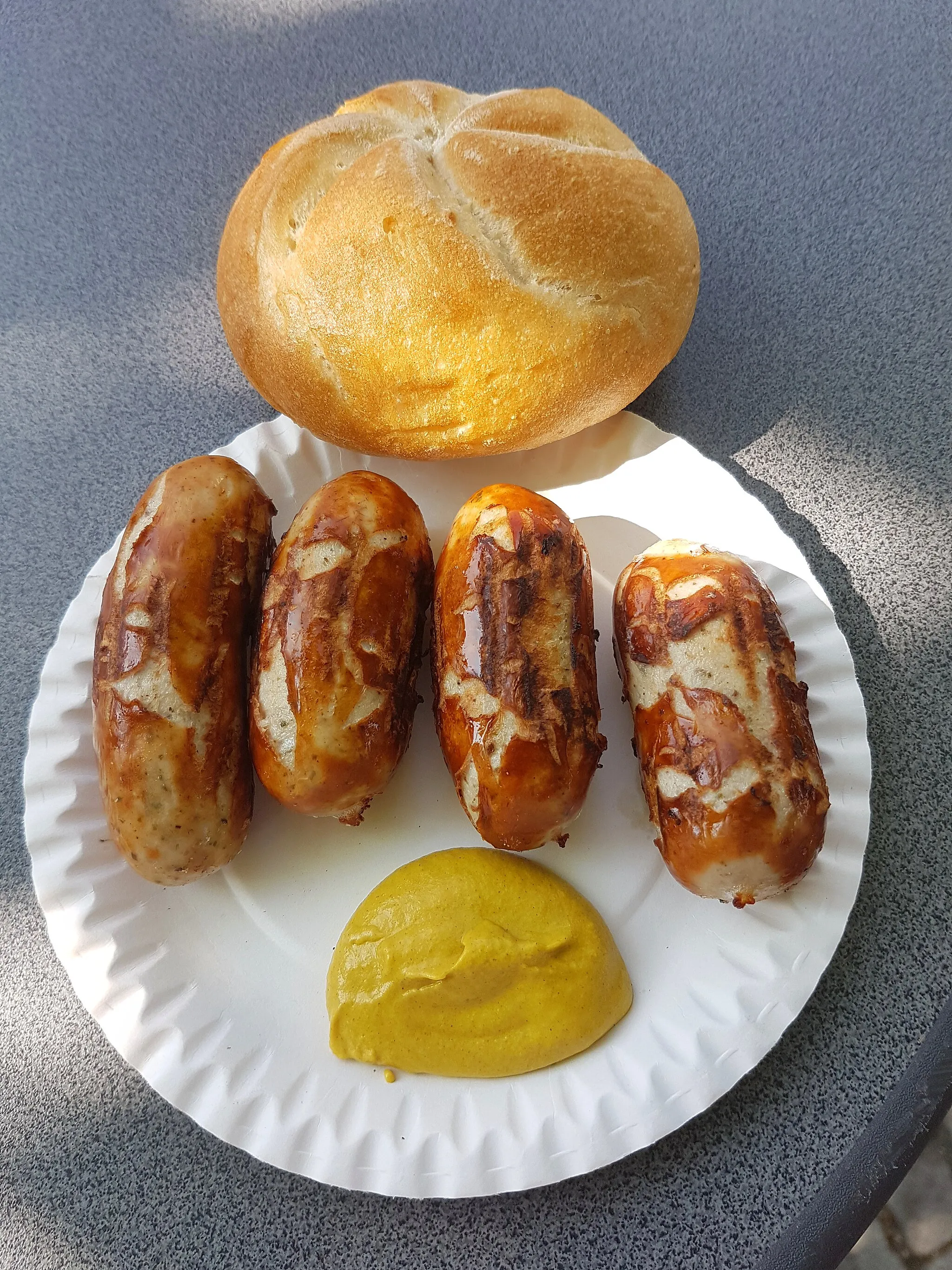 Photo showing: Original Brunner's sausages from the Brunner butchery in Landshut. The sausages are sold at snack stands in and around Landshut. They are grilled on charcoal and eaten with mustard and bread rolls or pretzels. One usually orders one pair, or 2 pairs of sausages. Photographed at a sausage stand in Ergolding opposite the town hall.