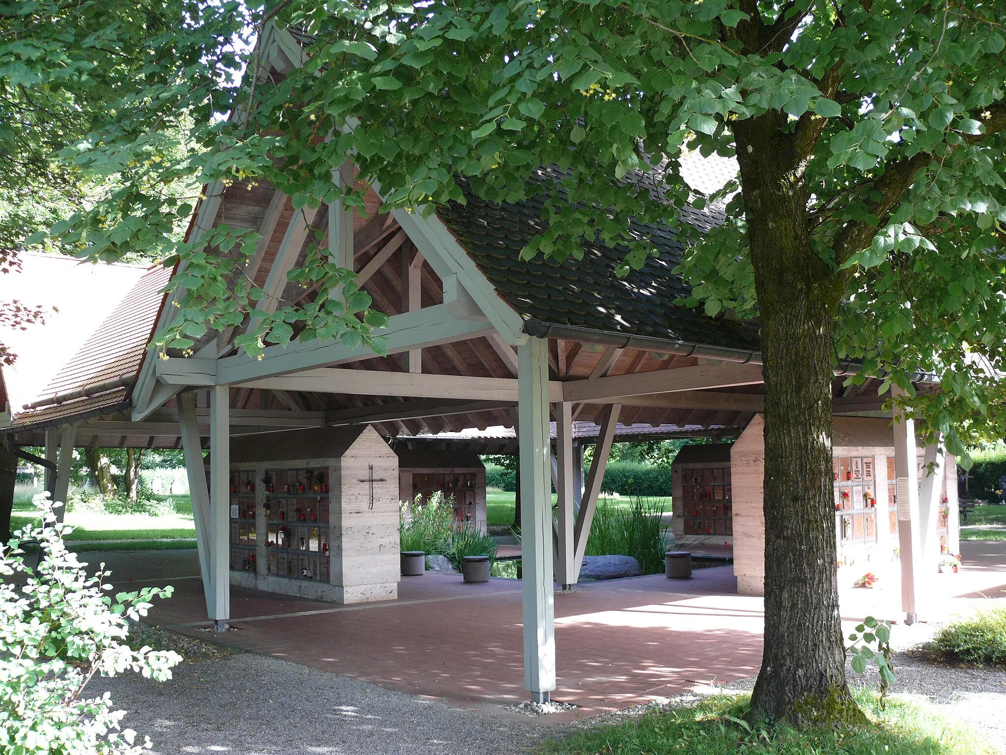 Photo showing: Weilheim, Friedhofweg 2, Friedhof: vier Urnenwände (Columbarien) unter breiten Schutzdächern, die sich um einen atriumartig in der Mitte liegenden Teich gruppieren. – Eine schöne, zeitgemäße und ebenso würde- wie stilvolle Lösung.