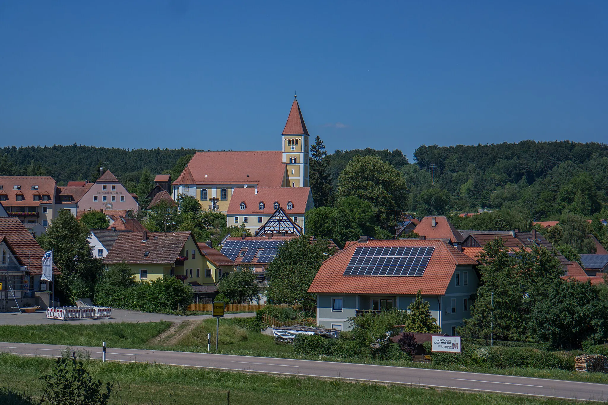 Photo showing: Ensemble Kirchberg Illschwang - Das Ensemble, das den Kirchberg von Illschwang umfaßt, bietet sich von Süden her in seiner eindrucksvollsten Fernsicht dar. Eingebettet in waldreiches Hügelland nutzt die Bebauung die Gegebenheiten einer Anhöhe aus: Unten am Bachlauf erdgeschossige Bauernhäuser mit Städeln, auf dem Höhepunkt die Simultan-Pfarrkirche St. Veit mit anschließendem Friedhof und kirchenburgartiger Ummauerung, umgeben vom evang.-luth. Pfarrhof und der fernwirksamen Giebelfassade des Gasthofes Weißes Roß. Am Fuß des Kirchbergs bilden wichtige Akzente die beiden gestaffelt angeordneten Fachwerkgiebel des Gemeindehauses und des evang.-luth. Pfarrstadels. Die 1109 erstmals erwähnte Pfarrkirche gehörte ursprünglich zum Kloster Kastl und wurde 1118 durch Markgraf Diepold III. seiner Neugründung Kloster Reichenbach übereignet. Zur Verwaltung des umfangreichen Besitzes in Illschwang errichtete das Kloster Reichenbach eine Propstei, welche bis zur Säkularisation bestand.