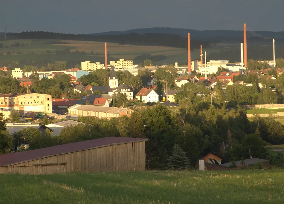 Photo showing: Blick auf einen Teil von Mitterteich aus westlicher Richtung. Die Kamine im Hintergrund gehören zur Firma Schott, die hier ein Werk betreibt. Links im Bild die alten Gebäude der ehemaligen Porzellanfabrik Rieber und am Horizon die Höhenzüge des Oberpfälzer Waldes. (2005)