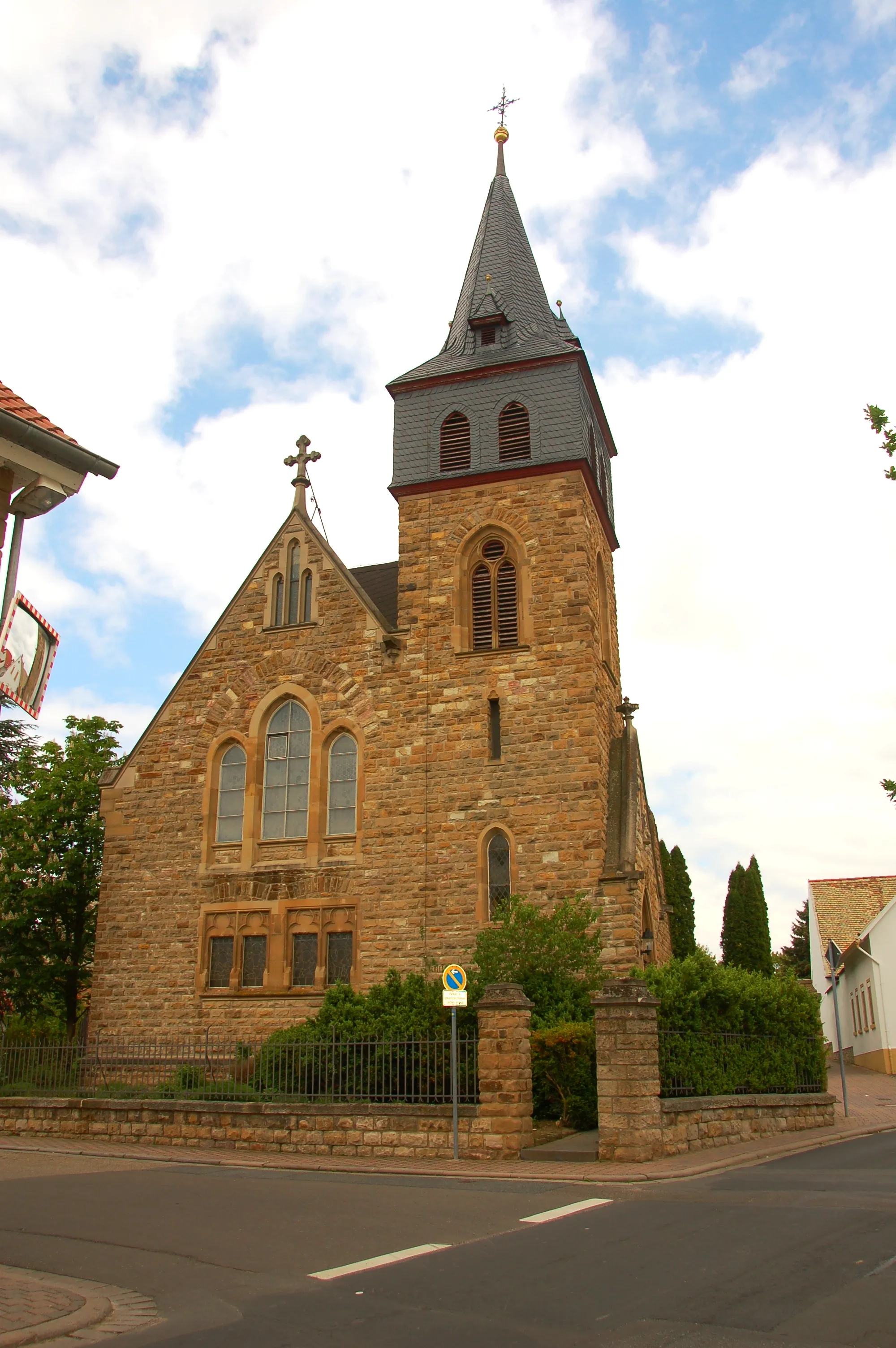 Photo showing: Neugotischer Saalbau, 1903/04. Das Gebäude wurde aus Flonheimer Sandstein nach einem Entwurf des Binger Architekten Johann Baptist Becker erbaut und am 9. Oktober 1904 eingeweiht. Der Kirchenraum hat eine gewölbte Stuckdecke, die mit Eisendrähten am Dachgebälk abgehängt ist. Zwei Doppelfenster auf der Westseite zeigen die vier Evangelisten Matthäus, Markus, Lukas und Johannes.