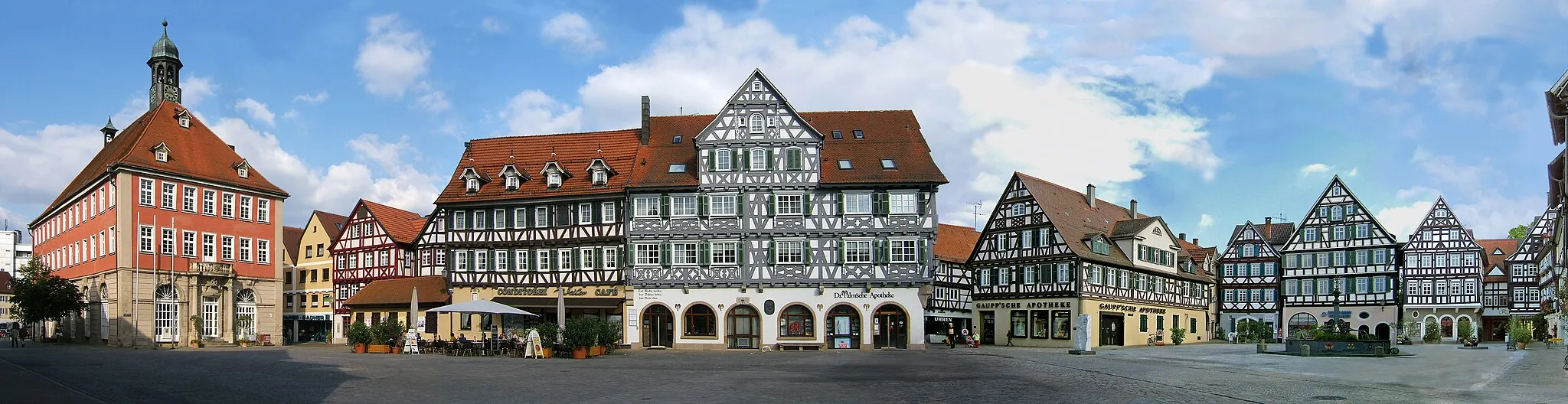 Photo showing: Marktplatz in Schorndorf, Deutschland,  mit dem Rathaus (links) und diversen Fachwerkhäusern, darunter Künkelinhaus, Palm'sche Apotheke, Gaupp'sche Apotheke und anderen, sowie  dem Marktbrunnen und den Skulpturen "Fortschnittschritt" von Hüseyin Altin (links des Brunnens) und "Das Gespräch" von Max Seiz (rechts des Brunnens.