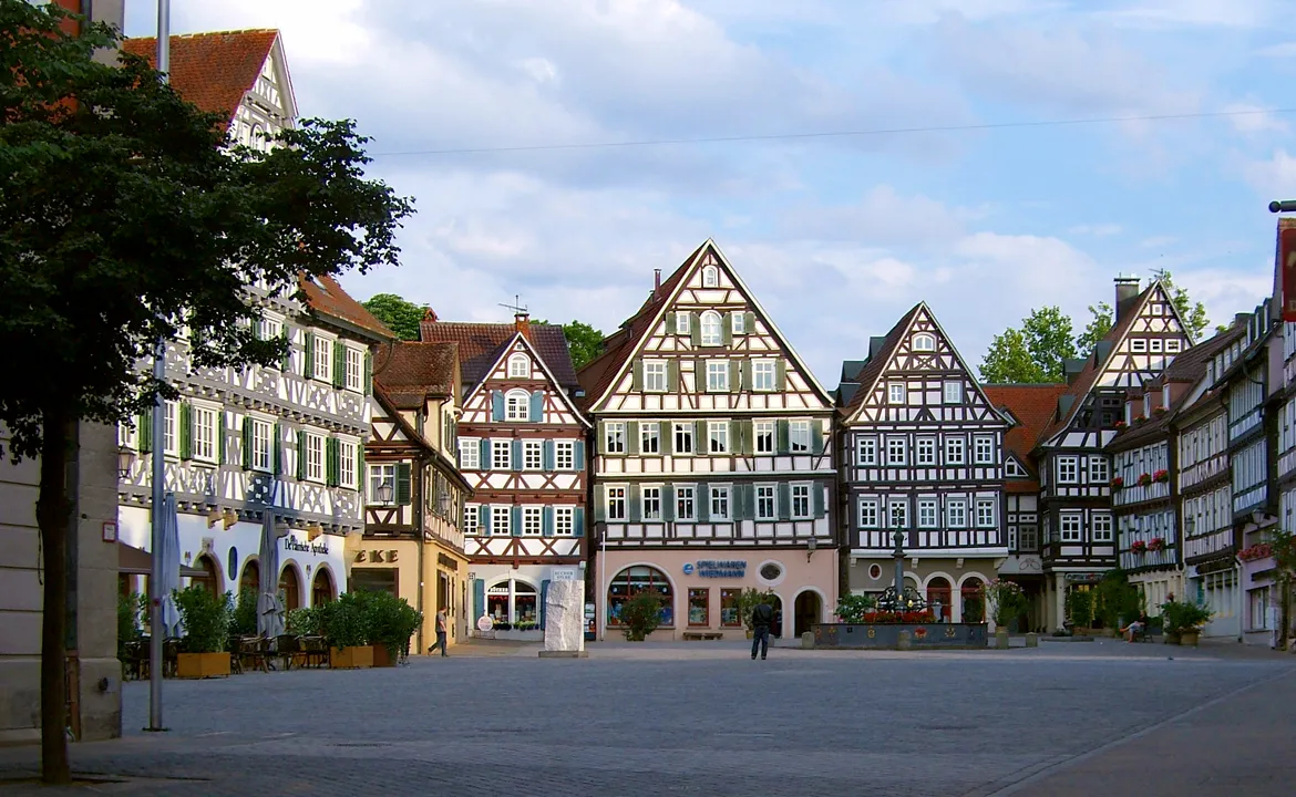 Photo showing: Der von Fachwerkhäusern umgebene Marktplatz in Schorndorf, Deutschland, mit dem  Marktbrunnen und der Skulptur "Fortschnittschritt" von Hüseyin Altin (links des Brunnens).