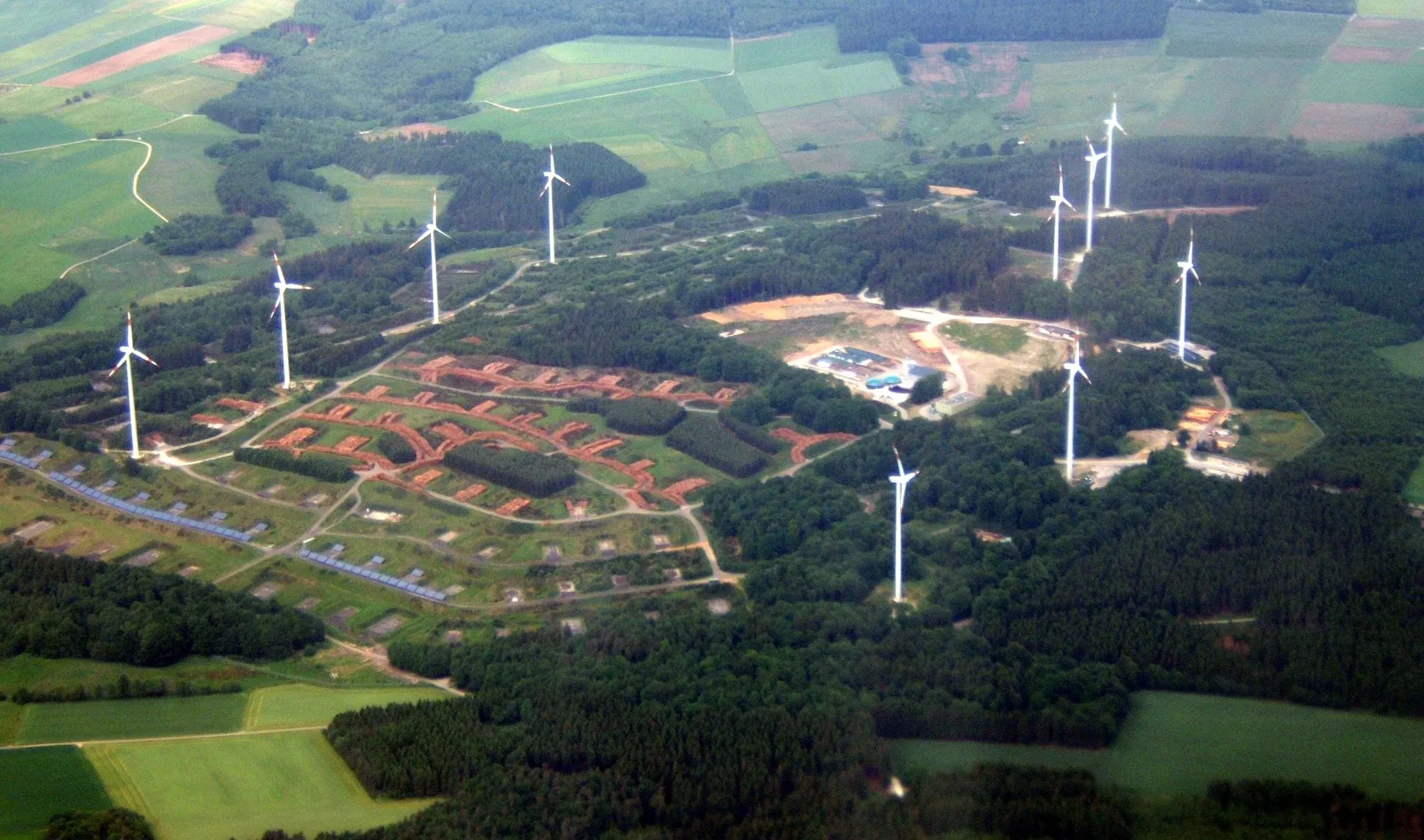 Photo showing: Aerial view of Energiepark Morbach (photovoltaics and wind turbines), near Morbach,  Bernkastel-Wittlich, Rhineland-Palatinate, Germany. Picture taken from a plane that was about to land at Frankfurt Hahn airport. (Formerly Hahn Air Base)  This property served as a Non-Nuclear Munitions Storage Area for the United States Air Force from the 1950's through the early 1990's. The Energiepark property is situated near the small towns of Wenigerath, Gonzerath, Heinzerath and Morbach. The wind turbines are Vestas V80-2MW units.