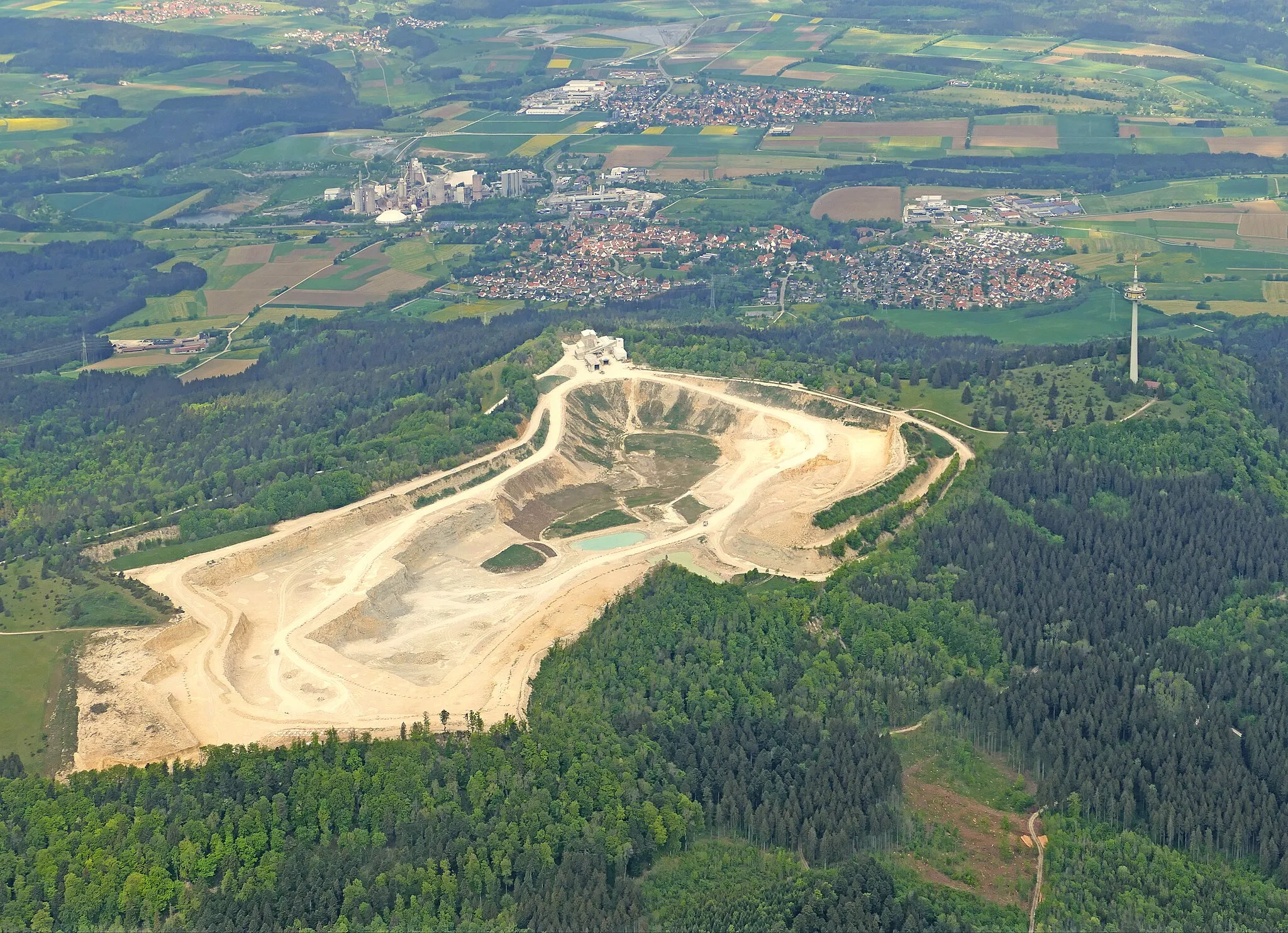 Photo showing: Aerial view of the quarry from the Dotternhausen cement plant, taken by a gyrocopter from an altitude of about 5700 feet. The picture was taken in an east-west direction. At the top left, next to Dotternhausen, the cement plant of LafargeHolcim Ltd. can be seen. One can also make out the Dotternhausen-Plettenberg material cableway between the cement plant and the quarry. On the northern tip of the approximately 1000 m high Plettenberg plateau is a 158 m high telecommunications tower (centre right).