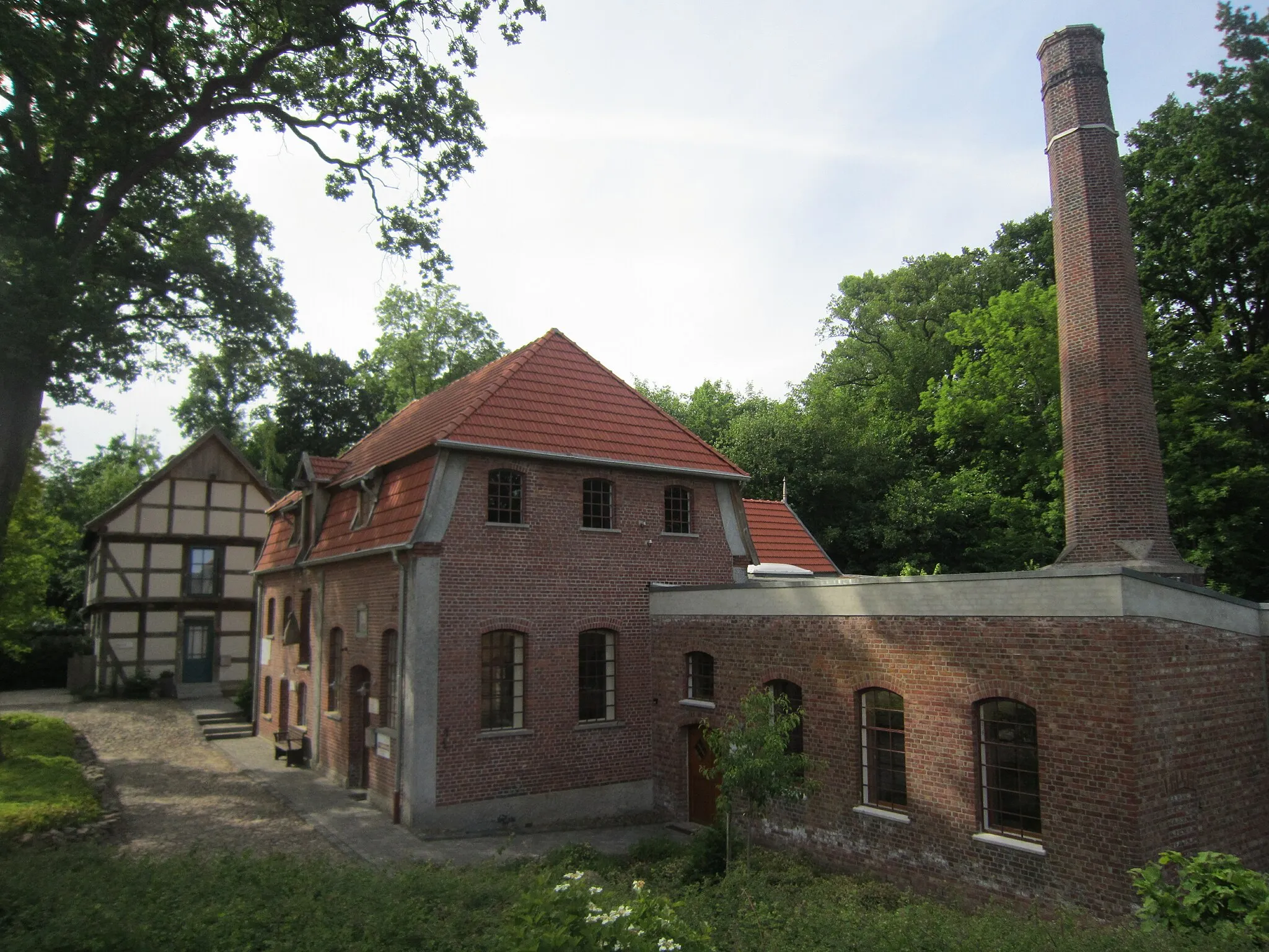 Photo showing: Das Industriedenkmal Bredemeyers Hof befindet sich an der Landesstraße von Vechta nach Twistringen in Goldenstedt (Landkreis Vechta in Niedersachsen). Nach umfangreichen Rekonstruktionsarbeiten wurde der Gebäudekomplex 2017 der Öffentlichkeit zugänglich gemacht. Er besteht seitdem aus einem Fachwerkspeicher aus dem Jahr 1722 (hinten links), einem Elektrizitätswerk aus dem Jahr 1907 (in der Bildmitte), einem Kesselhaus mit einem Schornstein (18 m) aus dem Jahr 1881 (vorne rechts), einer alten Getreidemühle mit drei Mahlwerken aus dem Jahr 1912, einer Wagenremise aus dem Jahr 1887 sowie einem Turbinenhaus und Teilen einer erstmals im 17. Jahrhundert erwähnten Wassermühle.