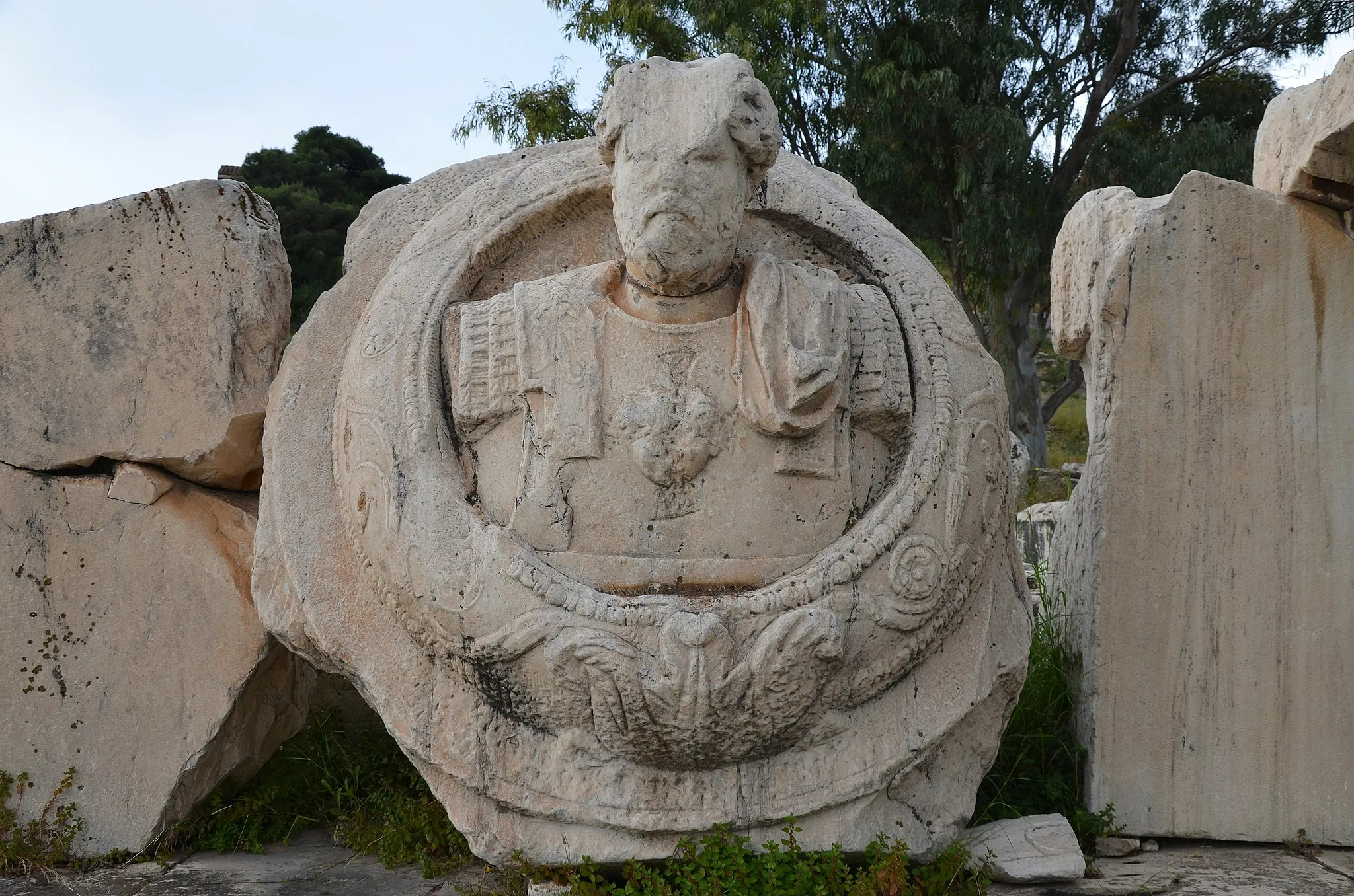 Photo showing: This cuirassed bust of an emperor was installed at the centre of the pediment of the Greater Propylaea.

Although the face is badly damaged, it is thought to be a portrait of the emperor Marcus Aurelius who built the Greater Propylaea.