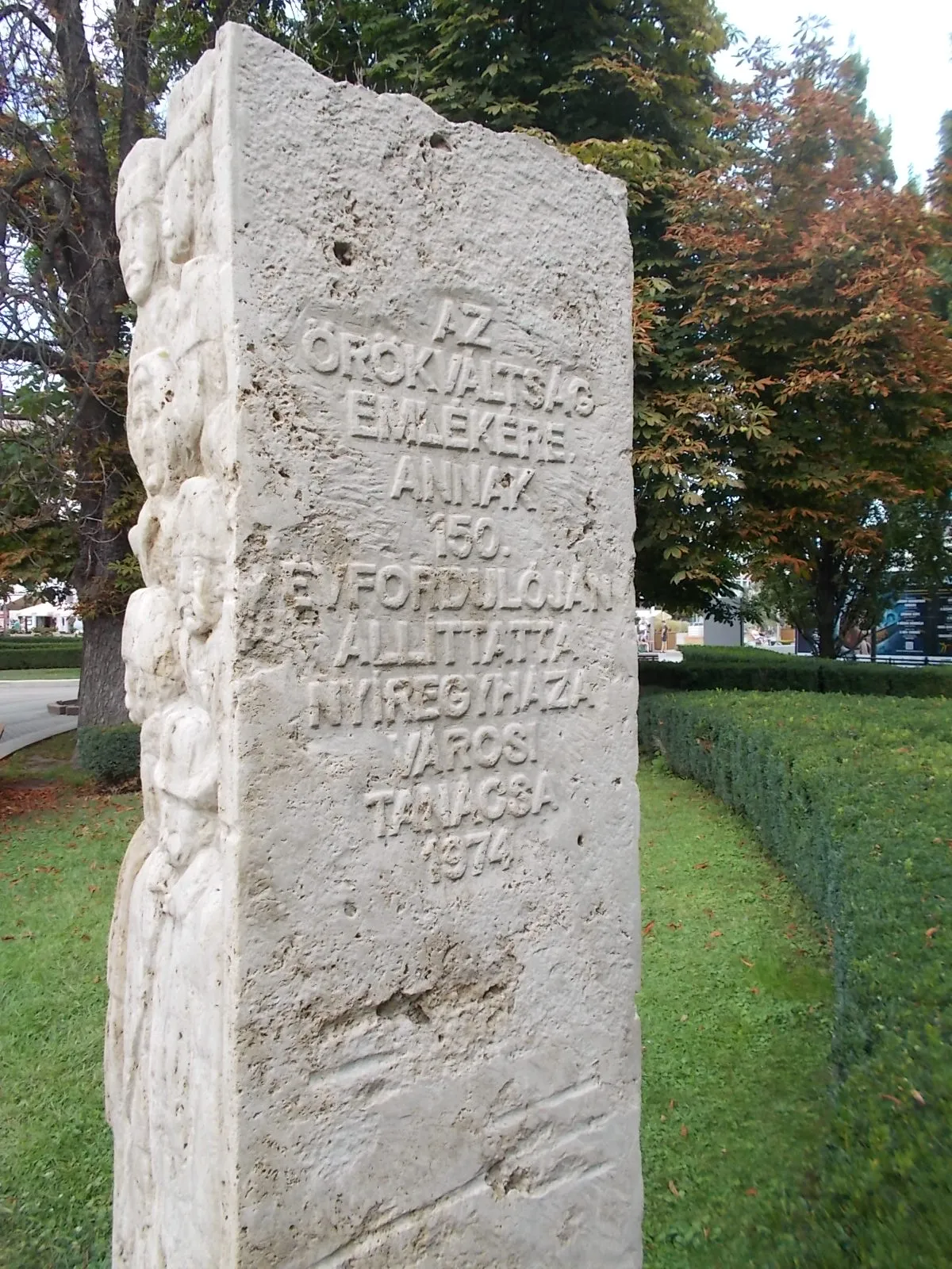 Photo showing: : Memorial column to the liberation of Dessewffy and Károlyi landlords. Because in 1824 the city bought free city status ( 150th anniversary, 1974 limestone works by Sándor Nagy ). Depicts: on the left side of the memorial column are the doubtful (peasants?) faces, on the right  side are trusting (peasants) faces. - Kossuth Square, Nyíregyháza, Szabolcs-Szatmár-Bereg County, Hungary.