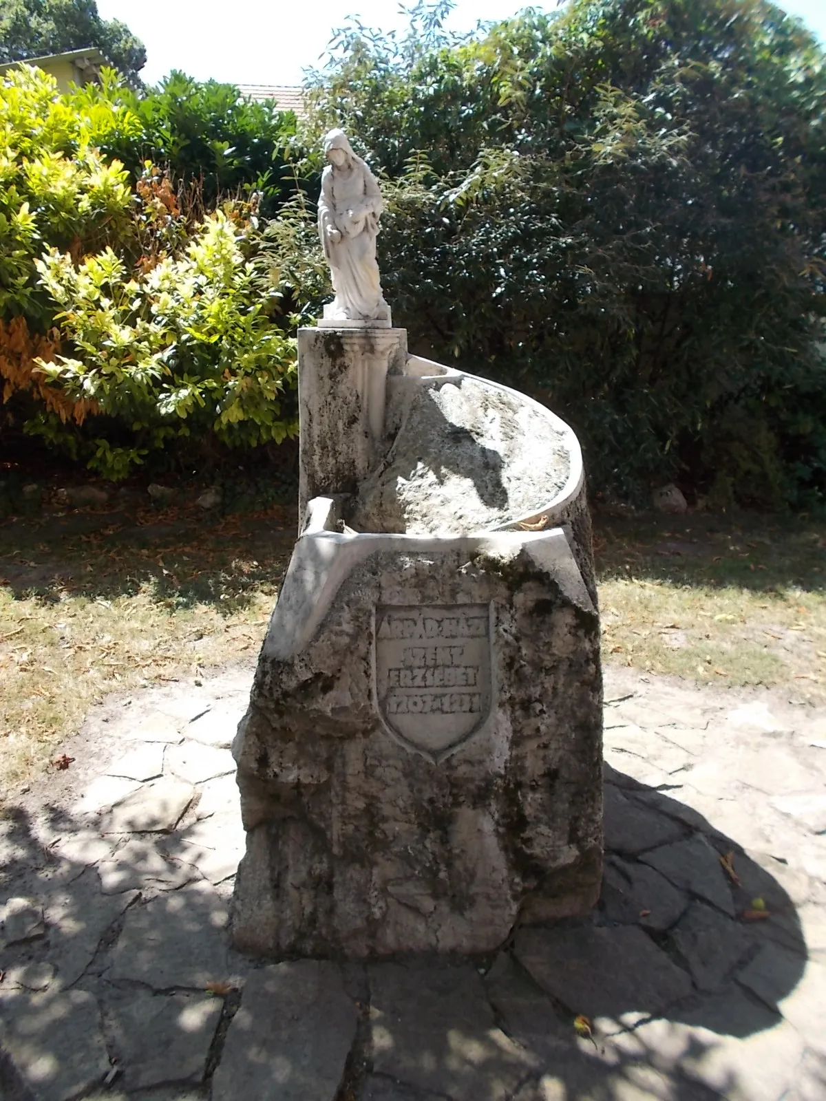 Photo showing: : Statue of Elisabeth of Hungary by László Bujtás (2007 work, replica /the original located in Győr/, limestone, for 800th Anniversary). She stands at the top of the castle-shaped pedestal, his eyes look into the depths in her apron are bread and roses. -  78 Fő Street (Route 8501), Lébény, Győr-Moson-Sopron County, Hungary.