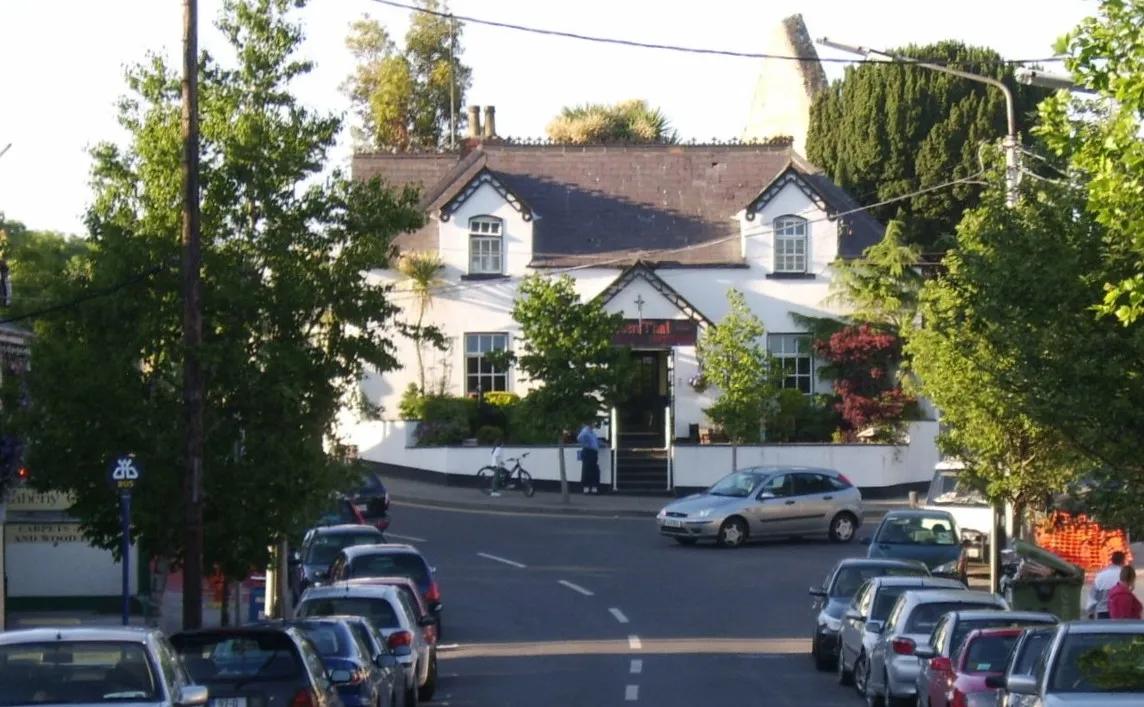 Photo showing: Part of Main Street, Raheny, Dublin, looking uphill towards a former school house (now a restaurant) which in turn backs on to the site of the old village church, (Old) St Assam's. The River Santry runs under the road in the foreground.
