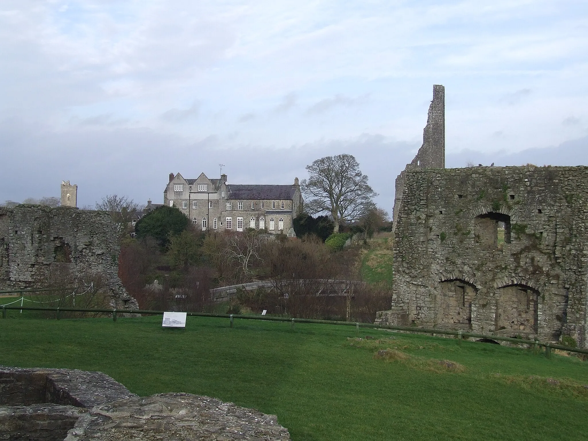 Photo showing: A view of Talbot Castle, Abbey Lane on the north bank of the River Boyne from the court of Trim Castle. A new bridge over the Boyne by French Lane is visible in centre. In the foreground are fore buildings of Trim Castle court. The ruins of the Royal Mint are on the right. The Solar or domestic quarters are on the left. To the top right, the bell tower of St Patrick's cathedral church is just visible.