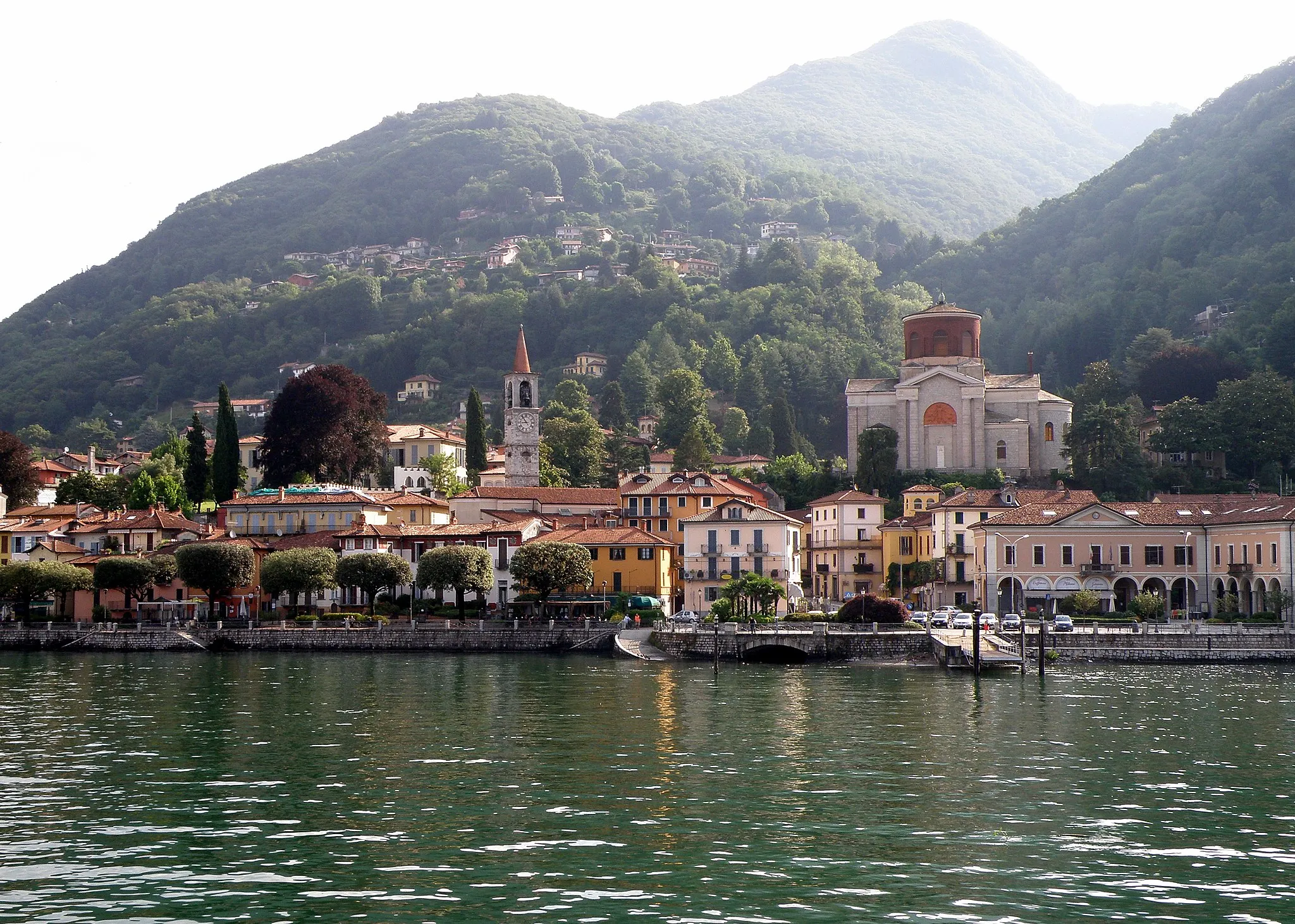 Photo showing: Laveno-Mombello (VA), vue prise depuis le bac (traghetto) de Verbania. À droite, église Saint-Ambroise (Chiesa di Sant'Ambrogio, dite Chiesa Nuova), de type néo-byzantin, juchée sur son esplanade surélevée. Au centre gauche, clocher élancé de l'église Saint-Philippe-et-Jacques (Chiesa di San Filippo e Giacomo, dite aussi Chiesa Vecchia). Bordant le quai tout à droite, l'ancienne mairie (devenu espace commercial) ; on entrevoit un peu la nouvelle mairie (la Villa De Angeli-Frua) derrière un arbre pourpre un peu à gauche du clocher de Saint-Philippe-et-Jacques. Au fond à droite, partiellement visible, le Sasso del Ferro. Au centre, dans le lointain, silhouette brumeuse du Monte Nudo. Nous regardons vers l'est-nord-est.