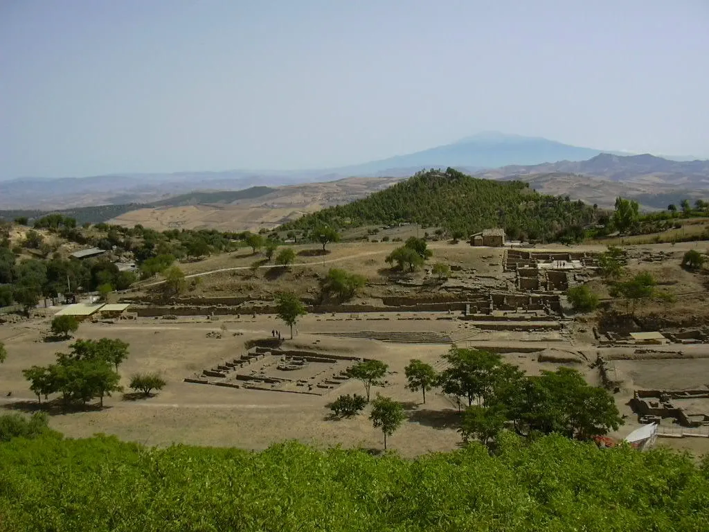 Photo showing: A view of Morgantina's Hellenistic agora. In the foreground the Macellum dating from the Roman period can be seen. In the background the Cittadella hilltop is visible, which was the location of Morgantina's Iron Age settlement. Mount Etna is seen in the far distance.