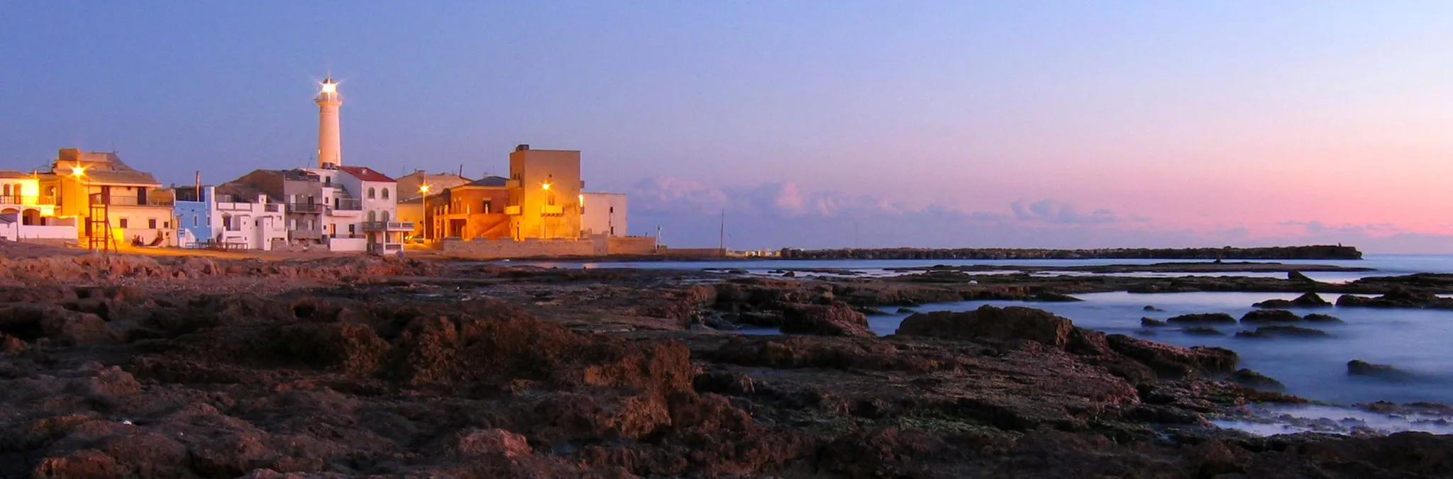 Photo showing: Punta Secca beacon and village skyline at sunset.
Author is Alessandro Zocco which has kindly agreed to share under GDFL license.
Photo was taken by him on Dec 26th, 2005.

Punta Secca: faro e profilo del villaggio al crepuscolo.
L'autore è Alessandro Zocco. La foto è stata scattata il 26 dicembre 2005.

Subito sotto il faro a destra è visibile la "casa del commissario Montalbano", utilizzata per le scene del film.