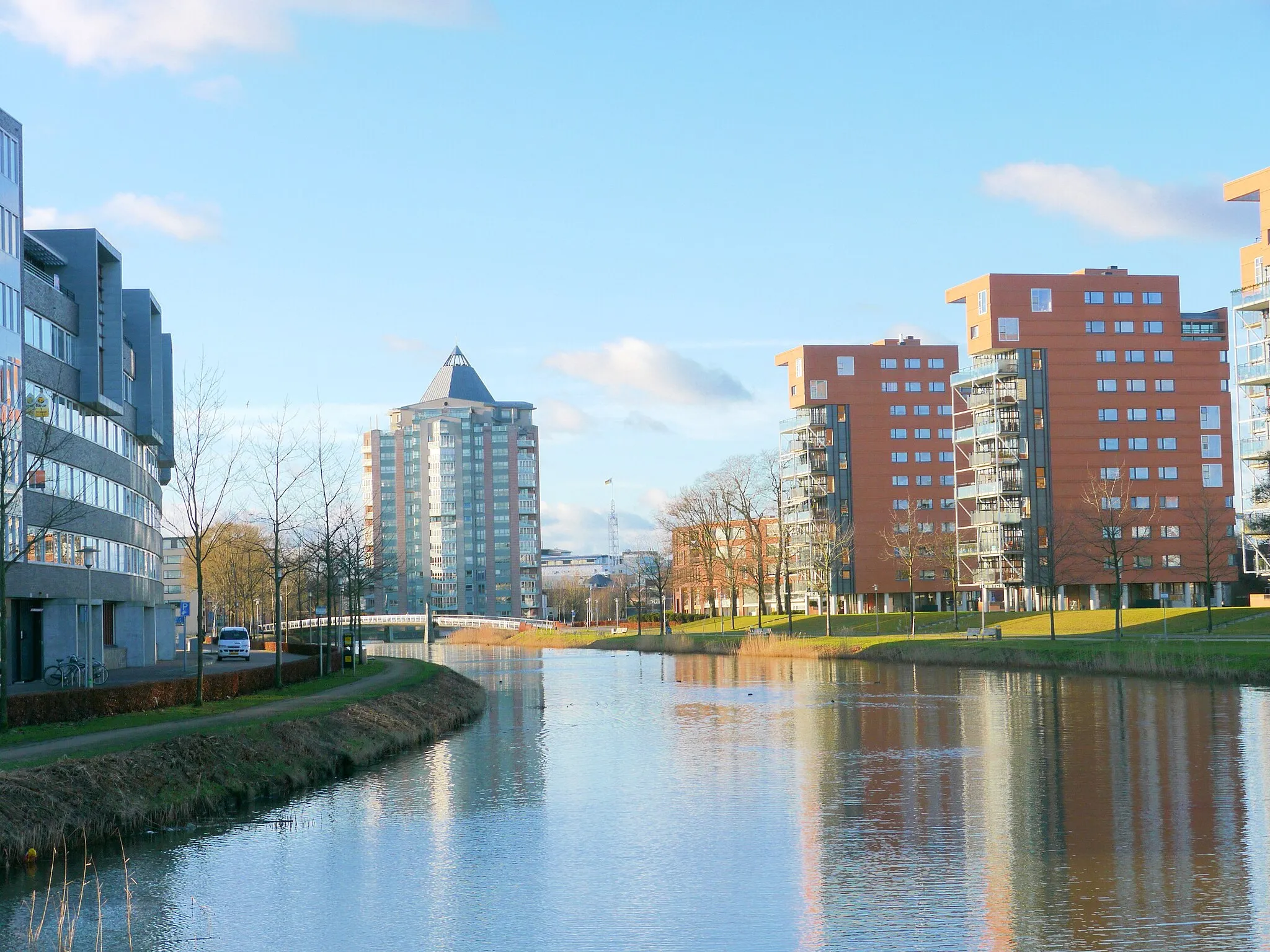 Photo showing: Grootschalig verbouwde kanaaloevers in Apeldoorn. Foto genomen vanaf de 'Welgelegenbrug'. In het midden de torenflat 'Het Potlood'. Juist daarvoor de brug 'De Freule'. Op de achtergrond, rechts van Het Potlood is het torentje van het stadhuis te zien.