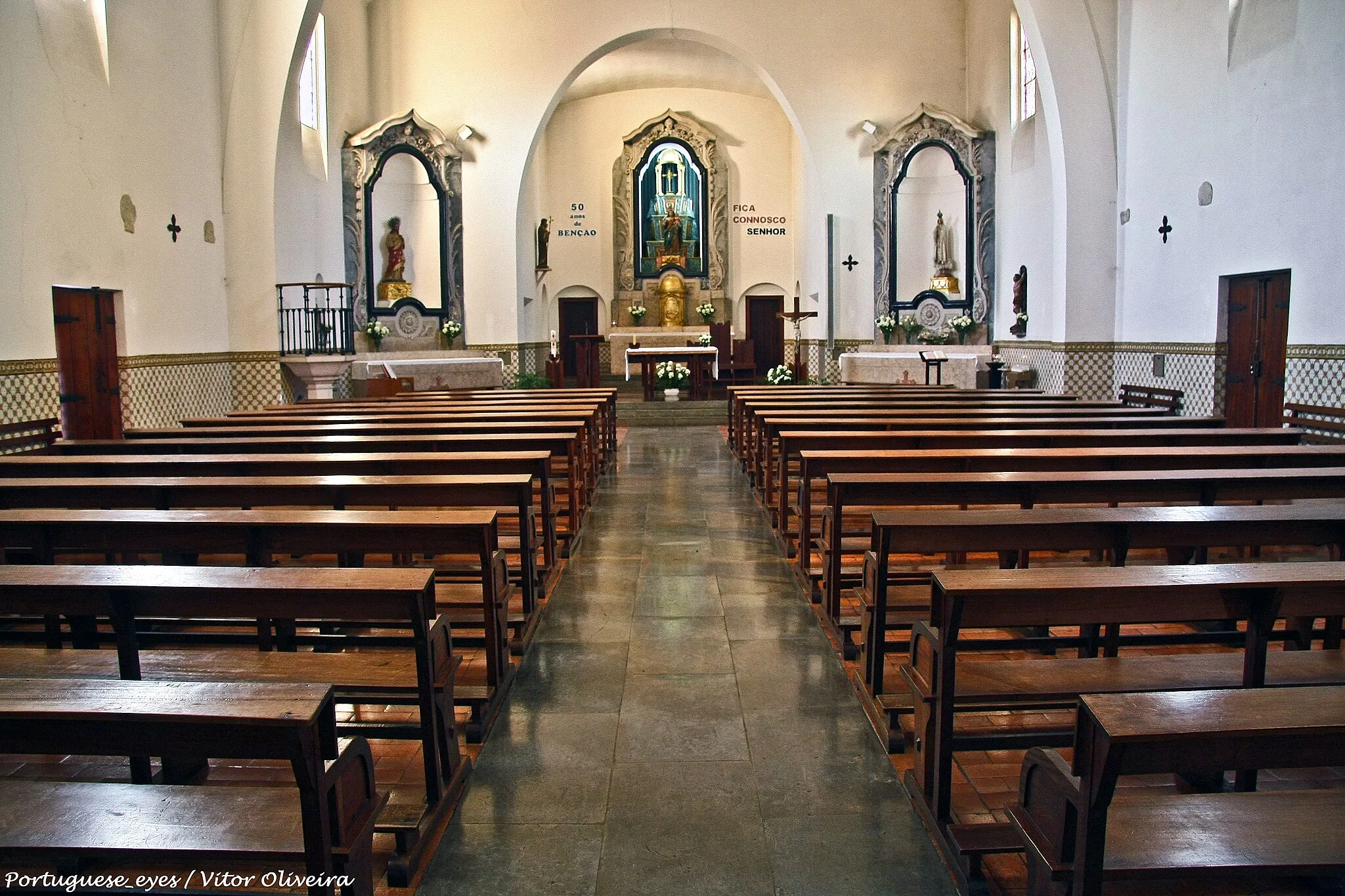 Photo showing: Instituída na Idade Média , possivelmente logo após a Reconquista Cristã da região a Norte do Tejo durante a segunda metade do século XII, Santa Maria de Aveiras aparece taxada em 100 libras no rol das « igrejas, comendas e mosteiros» que existiam em Portugal no ano de 1320, quando D. Dinis é autorizado pelo papa João XXII a receber o dízimo das rendas eclesiásticas para a burla de cruzada.
Por " Carta" de D. João I de 1401 e confirmada por D. Duarte em 1434, a par da jurisdição temporal de confirmação das autoridades e ofícios locais, a jurisdição eclesiásticas e a apresentação do prior de Santa Maria de Aveiras passou a ser prerrogativa do bispo e depois arcebispo D. João Afonso Esteves de Azambuja.
Por morte deste em 1415, passou a igreja a D. Isabel Pires ou de Azambuja, Comendadeira de Santos, da Ordem de Santiago da Espada, dando início ao Padroado das Comendadeiras da ordem de Santiago, que passaram também a deter a jurisdição da Vila, como o confirma o título do Foral Manuelino do século XVI.
Ainda em 1834 a Comendadeira de Santos se intitulava Senhora donatária da Vila de Aveiras e do lugar de Vale Paraíso e Padroeira da Igreja e Reitoria de Aveiras de Cima e vigararias das Vilas de Aveiras de Baixo e do Cartaxo.
Nas Memórias Paroquiais de 1758, o Cura João Pena Morais , confirma, que era « donatária da Vila de Aveiras de Cima a Excelentíssima Comendadeira de Santos Novos da cidade de Lisboa» e « o pároco era vigário» apresentado pela mesma Comendadeira .« O orago e titular da Igreja Matriz è Nossa Senhora da Purificação» e «tem três altares, um da dita Senhora e do Santíssimo Sacramento, outro do Menino Deus, outro de Nossa Senhora dos Milagres; não tem naves; tem uma Irmandade das Almas». Um século depois é instituída a Irmandade do Santíssimo Sacramento, cujo Compromisso foi aprovado em 1859.
Entre os inúmeros monumentos funerários resgatados das fundações do templo, testemunhos que documentam as memórias medievais de Santa Maria de Aveiras, sobressaem as estelas lavradas com simbólica cruciforme, ou cabeceiras de sepultura, apresentadas na galilé e corpo do templo e, as sepulturas com epitáfio em letra gótica. Destas, tem o destaque o fragmento da sepultura de Pêro Paes, datada do ano de 1552.
Monumentos simbólicos resgatados do esquecimento, a secular igreja de Nossa Senhora da Purificação de Aveiras de Cima foi descrita em 1751, no Dicionário Geográfico do Padre Luís Cardoso como um « templo antigo e tosco».
A degradação, o peso do tempo secular ditaram a primeira tentativa de reerguer e dignificar o templo medieval, em finais do século XIX.
Como a igreja estava muito arruinada e de difícil reparação, tornou-se necessário construir outra, tendo-se conseguido o subsídio de um conto de reis do Governo, em 1897. Existia então uma Comissão para a edificação de um novo templo a erigir no centro da povoação, numa propriedade de José Sequeira e depois de António Fialho Henriques. Caído por terra tanto o ensejo de uma nova edificação como demolido o templo antigo e tosco, bem como o seu sucedâneo, vão passar-se mais de 60 anos para se avançar com um terceiro plano de edificação, dado o anterior espaço de culto ser um templo inacabado e tecnicamente identificado como uma estrutura cheia de perigos.
É deste modo que em 1953 têm início as obras de construção da «nova» igreja, depois de uma enorme envolvência e mobilização colectiva do povo.
Vários peditórios, o memorável cortejo de oferenda realizado a 11 de Novembro de 1952 e de um outro chamado «cortejo da boa vontade» no próprio dia da inauguração, quermesses, etc. através de uma Comissão de que faziam parte os padres Luís A. de Oliveira Mendes e António José dos Santos, Francisco de Barros Júnior, Francisco de Mendia, José Rodrigues Batoreo, João Goulart de Medeiros, Alfredo Martins Pinto, Ezequiel Pereira Leitão, Joaquim Martins Maurício, José Duarte Mendes, Joaquim Manuel Leandro, Joaquim Manuel Lamas e José Félix Assucena, foram as iniciativas principais e os rostos que ficaram como memória futura.
Da autoria do arquitecto Vasco Morais de Palmeira (Regaleira), a actual Igreja Matriz de Nossa Senhora da Purificação de Aveiras de Cima, foi solenemente inaugurada a 20 de Dezembro de 1959, por Sua Eminência o Senhor Cardeal Patriarca de Lisboa, D. Manuel Gonçalves Cerejeira.
E a «nova» Igreja honrou como nunca a sua padroeira nos dias 26,27,e 28 seguintes, através de " Grandes Festividades" em honra de Nossa Senhora da Purificação e do Mártir S. Sebastião, num derradeiro esforço da Freguesia para saldar as contas de obra tão grandiosa.
Ficava serenizada a inquietação que tanto atormentava o então Prior Luís A. de Oliveira Mendes que a propósito então escreveu:
Não celebrara ainda as suas bodas de ouro ( após a reconstrução ) a velha igreja de Aveiras de Cima quando nela celebrei a Santa Missa, pela primeira vez, a 14 Novembro de 1948, mas já as paredes fendidas, os estuques caídos do tecto, os vidros estilhaçados faziam prever um fim prematuro. Para ela os técnicos não viram outro remédio senão apeá-la e reedificá -la novamente. Mas antes era necessário implantá-la na alma dos crentes... e depositar este plano tão arrojado nos corações de todos os aveirenses.
A ela, a esta nova Igreja acorrerão as promessas de uma Aveiras nova !
Todos os aveirenses sem excepção marcaram a sua presença e em cada pedra, em cada prego está uma gota de sangue e de vida de cada um dos habitantes desta paróquia.
Que esta obra e todas as que estão associadas e promovidas pela Paróquia de Nossa Senhora da Purificação de Aveiras de Cima, continuam ao serviço cultural e social da comunidade, como símbolos espirituais e materiais impressos no coração e na memória afectiva de cada um e de todos os aveirenses porque fazem parte integrante do maior património cultural comum a que o Homem chama História enquanto projecto colectivo que em cada Presente constitui um marco onde se escreve o Futuro.

Síntese da História Paroquial de Nossa Senhora da Purificação de Aveiras de Cima, da autoria do historiador - José António Machado Pereira www.freguesia-aveiras-cima.pt/jf/index.php?option=com_con...