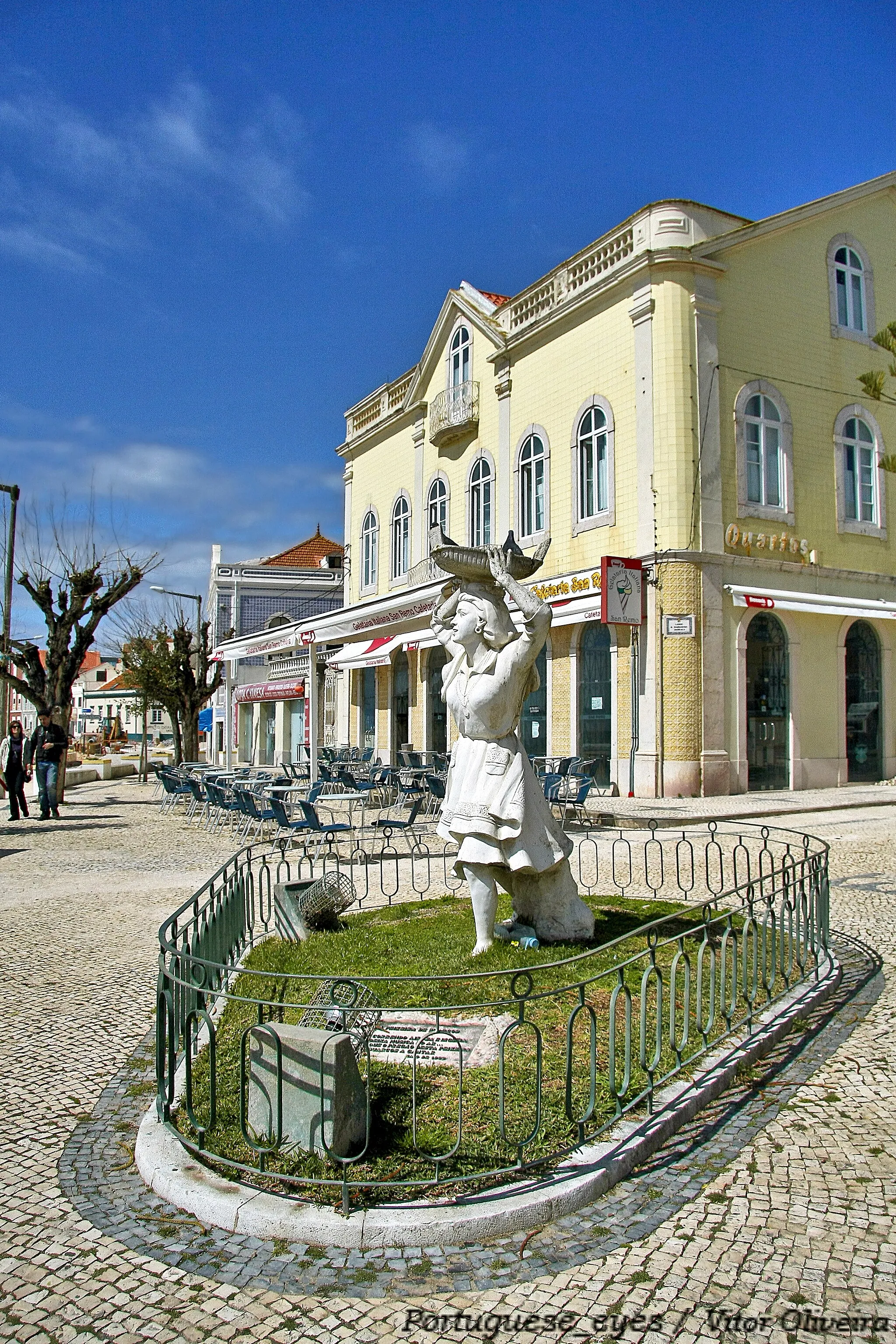 Photo showing: Autor: Cabral Antunes
Localização: Figueira da Foz, Buarcos, Largo Dª Maria Barraca.
Data de Inauguração: 10.05.1966
Promotor: Comendador Mário Barraca
Materiais: Cimento
Dimensões: 230 x 95 x 100cm
Descrição/ Tema: Estátua em betão pretende homenagear as peixeiras de Buarcos, assenta num pequeno espaço ajardinado criado no Largo de Dª Maria Barraca. Constituída por uma figura feminina, de influências naturalistas, exibe um grande dinamismo formal com linhas sinuosas que lhe transmitem força e movimento. Cabral Antunes apresenta a figura com indumentária característica das peixeiras, com o pormenor do avental bordado, e, com uma atitude como se estivesse a caminhar apressada, segurando com ambas as mãos uma canastra que “leva à cabeça”, numa expressão que evoca o apregoar do peixe.
Junto à estátua tem uma lápide com uma quadra inscrita do poeta figueirense José Mendes Pinto “Correndo airosa e ligeira / Deixa música no ar…/ Que o pregão desta peixeira / É Buarcos a cantar / Maio de 1996”.
Historial: Em 1996, o Comendador Mário Barraca oferece a Buarcos a estátua de homenagem à peixeira que encomendara ao escultor Cabral Antunes.
Bibliografia: NUNES, Mário, Estátuas de Coimbra, Coimbra 2005;

- Informações prestadas pela Câmara Municipal da Figueira da Foz www.culturacentro.pt/museuit.asp?id=34