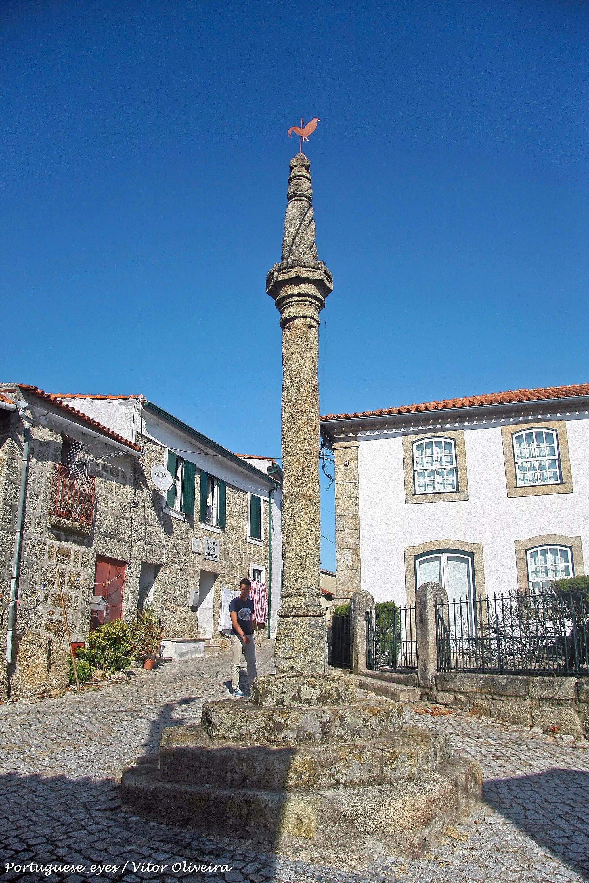 Photo showing: Estrutura em cantaria de granito, composta por soco de quatro degraus escalonados, com base paralelepipédica quadrangular de vértices chanfrados superiormente. Plinto circular com toro, onde assenta fuste torso de quatro vergas espiraladas encimado por gola côncava entre molduras. Ábaco saliente, oitavado, com anel circular, remate cónico, torso, de dois registos escalonados, separados por gola estreita, finalizando em pequeno coruchéu de cinco esferas sobre anel. Sobre a esfera superior um galo catavento. A um terço da altura do fuste, dois furos tapados com gesso, indicam onde estiveram cravados os ferros de sujeição. www.monumentos.gov.pt/Site/APP_PagesUser/SIPA.aspx?id=2558