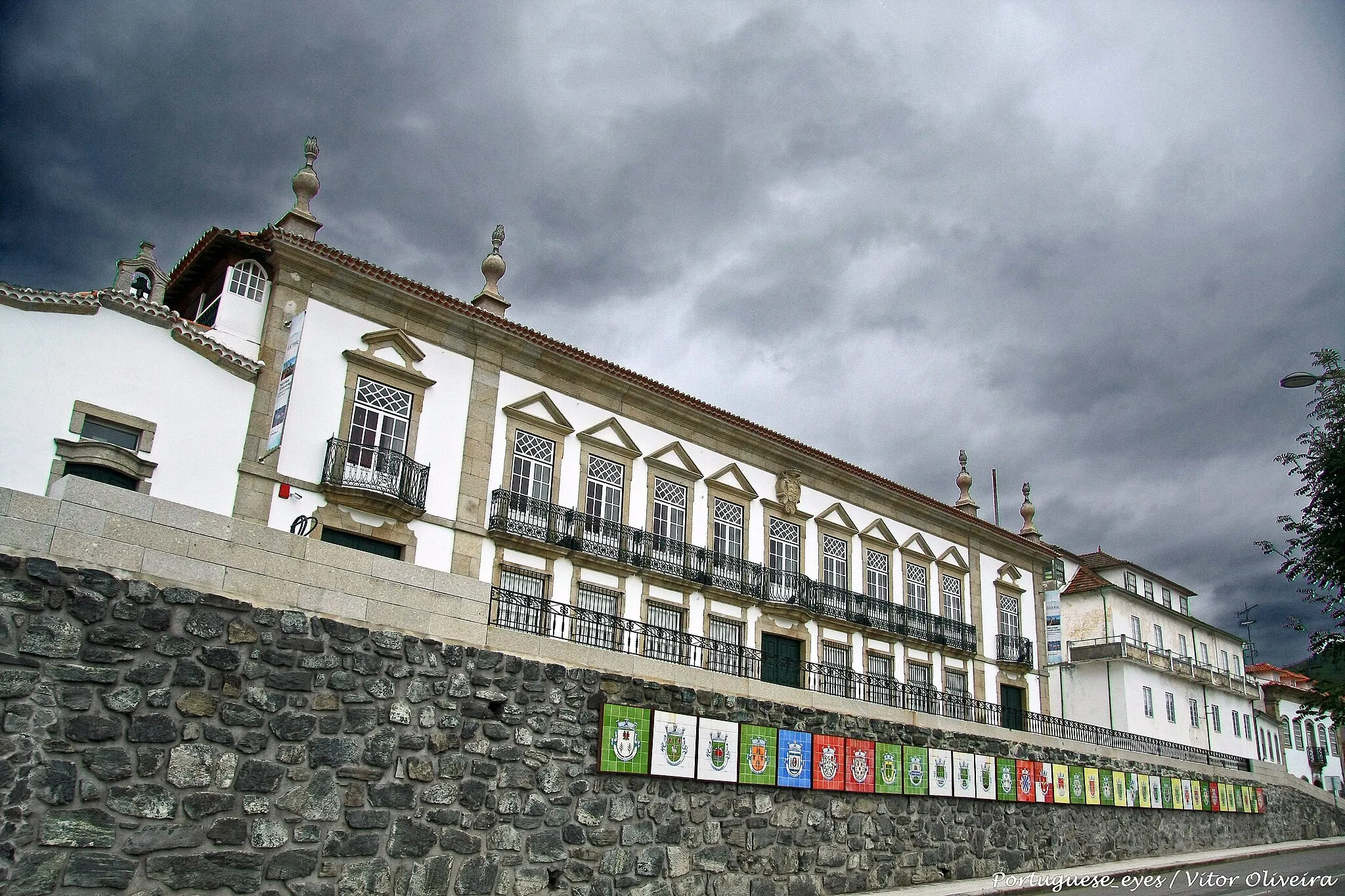 Photo showing: O solar dos Condes de Vinhais foi edificado na rua Nova, principal eixo viário da vila de Vinhais. Trata-se de um monumento setecentista, exibindo na sua fachada todo o dinamismo barroco. O brasão pode ter sido colocado após 1847, ao centro do alçado. Neste ano Dona Maria concedeu o título de Conde a Simão da Costa Pessoa. Sendo nesta altura palco de uma reestruturação, como forma de tornar o edifício mais digno do título então adquirido pelo proprietário.

Ostenta uma planta longitudinal com quantidade articulada e cobertura, feita de telha, de quatro águas. A frontaria tem um largo corpo central, acompanhado por dois corpos mais estreitos isolados por pilastras sobrepujadas por urnas. Os corpos laterais têm porta de verga recta no primeiro piso e janela de sacada com balaustrada de ferro semicircular, cornija saliente e frontão triangular no segundo. O corpo central tem um portal axial no primeiro piso e quatro janelas de avental gradeadas e, no segundo, janelas de sacada corrida, com cornija saliente e frontão triangular, excepto a central que apresenta uma varanda encimada pela pedra de armas dos condes de Vinhais. A capela particular fica do lado esquerdo, da exoração de São Caetano, e por trás a área de serviço. No andar nobre existem duas salas que comunicam com outras duas de inferiores simetrias. Estes aposentos eram adornados com pinturas bucólicas, encontrando-se hoje muito degradadas. www.turismovinhais.com/?patrimonio=solar-dos-condes-de-vi...