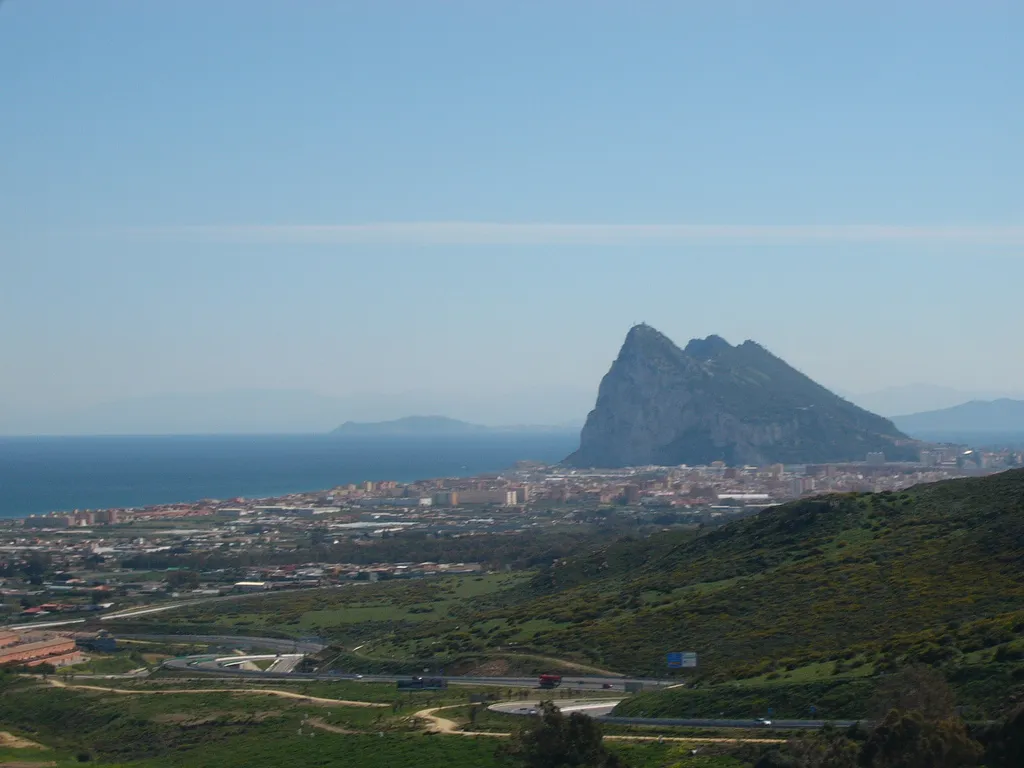 Photo showing: The Rock of Gibraltar and La Línea from the Campo de Gibraltar. Sierra Carbonera in the foreground, on the right. Africa in the background. The road is regional road A-383