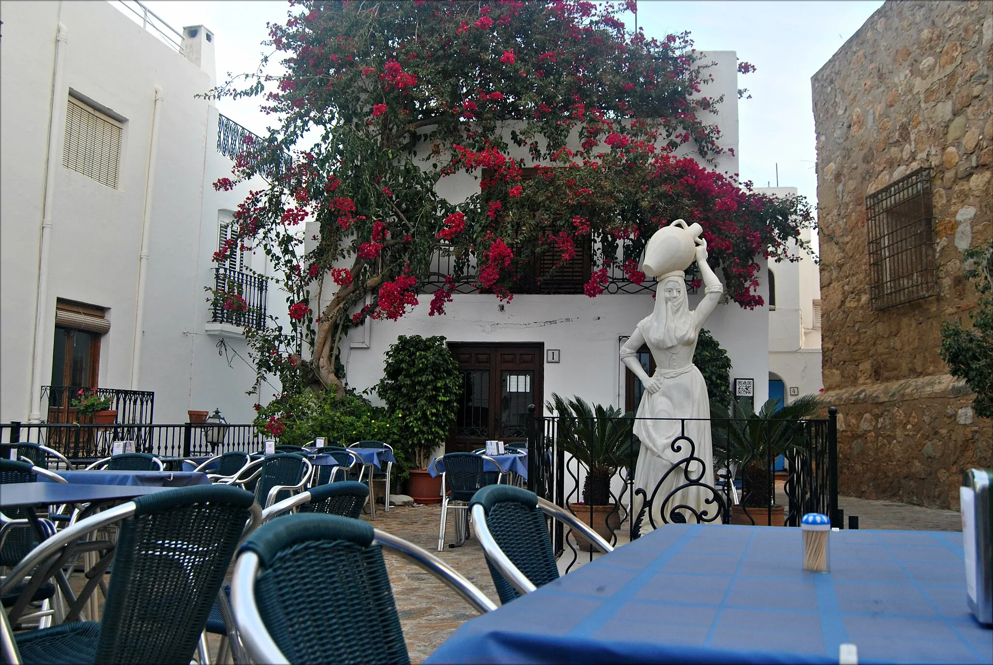 Photo showing: The Statue of Mojaquera is located opposite the Church of Santa Maria in Mojácar. The marble statue depicts a woman  dressed in the traditional costume of old, holding the Arab scarf in her teeth and covering part of her face, carrying a pitcher of water on her head for the towns inhabitants.
I added this write up from a website that describes it better...
The Mojaquera
While your getting lost in the winding streets of Mojacar, look out for a certain young lady. It's not often you come across a monument to a woman in Spain. They tend to be either stern looking military heroes, or long forgotten bishops. Mojacar though, has put up a monument to some very important women who over the centuries lugged water from  The Mojaquera the Moorish fountain at the foot of the village all the way to the top.

If you get a bit of puffed out on your way up there, spare a thought for the Carmens and Marias who with a brimful clay pot as headgear, negotiated the winding tracks to the top, headscarf held firmly in place with clenched teeth. The tiny pitcher-toting white marble statue of the Mojaquera stands in front of the church sporting typical dress, her face covered. Arab style. Santa Maria, the church itself, isn't the usual fancy wedding cake construction you often find in Spain, but a former fortress made of huge stone slabs. from this site